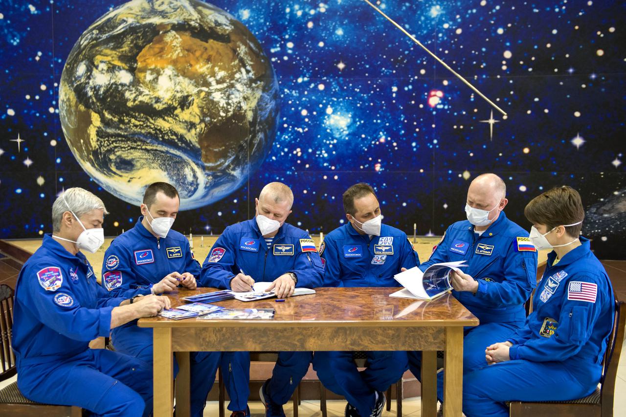 From left to right, Expedition 65 prime crew members NASA astronaut Mark Vande Hei, and Russian cosmonauts Pyotr Dubrov, and Oleg Novitskiy of Roscosmos, are seen with backup crew members Russian cosmonauts Anton Shkaplerov and Oleg Artemyev, and NASA astronaut Anne McClain while signing mission books after the final Soyuz MS-18 spacecraft fit check, Sunday, April 4, 2021 at the Baikonur Cosmodrome in Kazakhstan. The prime crew is scheduled to launch to the International Space Station aboard the Soyuz MS-18 spacecraft on April 9. Photo Credit: (NASA/GCTC/Irina Spector)
