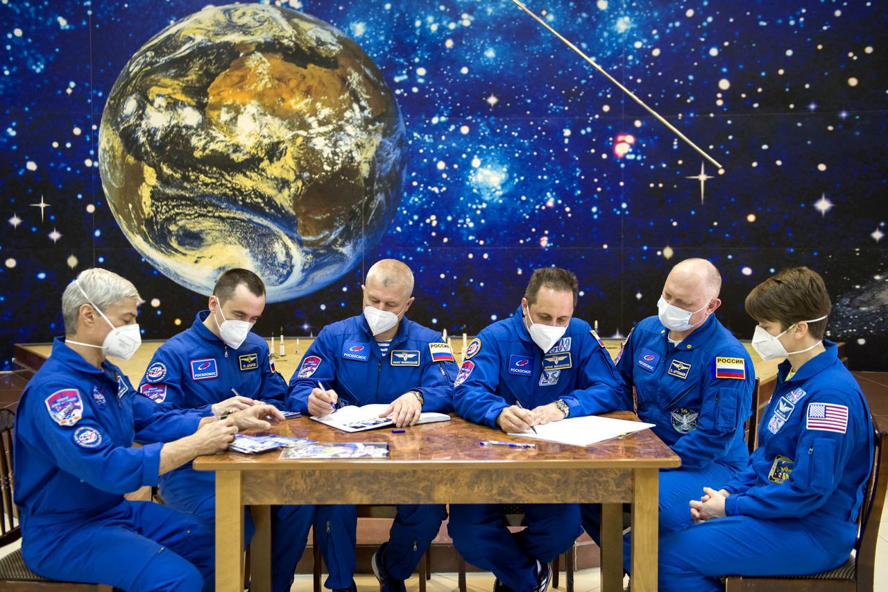 From left to right, Expedition 65 prime crew members NASA astronaut Mark Vande Hei, and Russian cosmonauts Pyotr Dubrov, and Oleg Novitskiy of Roscosmos, are seen with backup crew members Russian cosmonauts Anton Shkaplerov and Oleg Artemyev, and NASA astronaut Anne McClain while signing mission books after the final Soyuz MS-18 spacecraft fit check, Sunday, April 4, 2021 at the Baikonur Cosmodrome in Kazakhstan. The prime crew is scheduled to launch to the International Space Station aboard the Soyuz MS-18 spacecraft on April 9. Photo Credit: (NASA/GCTC/Irina Spector)