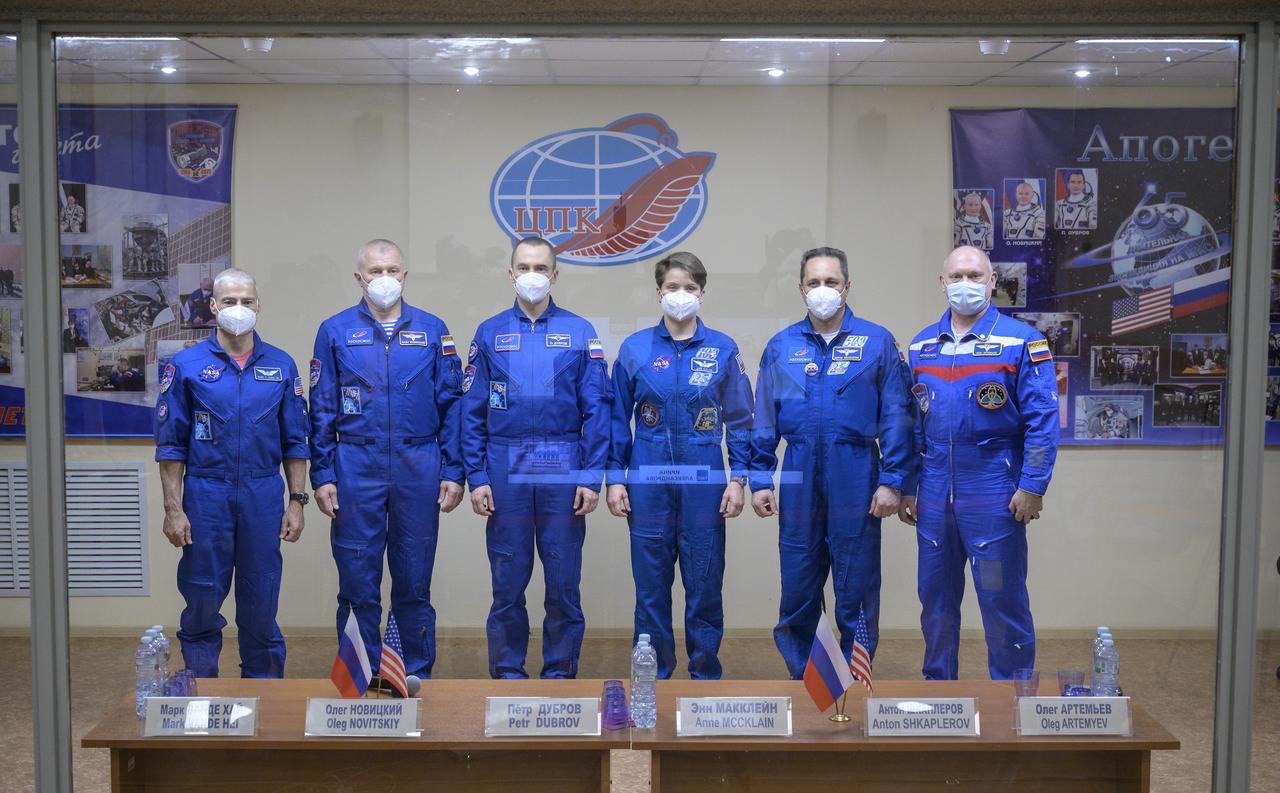 Expedition 65 NASA astronaut Mark Vande Hei, left, Roscosmos cosmonauts Oleg Novitskiy and Pyotr Dubrov, along with backup crew members Anne McClain of NASA, and Roscosmos cosmonauts Anton Shkaplerov and Oleg Artemyev, right, are seen in quarantine, behind glass, during a press conference, Thursday, April 8, 2021 a the Cosmonaut Hotel in Baikonur, Kazakhstan. The prime crew is scheduled to launch to the International Space Station aboard the Soyuz MS-18 spacecraft on April 9.  Photo Credit: (NASA/Bill Ingalls)