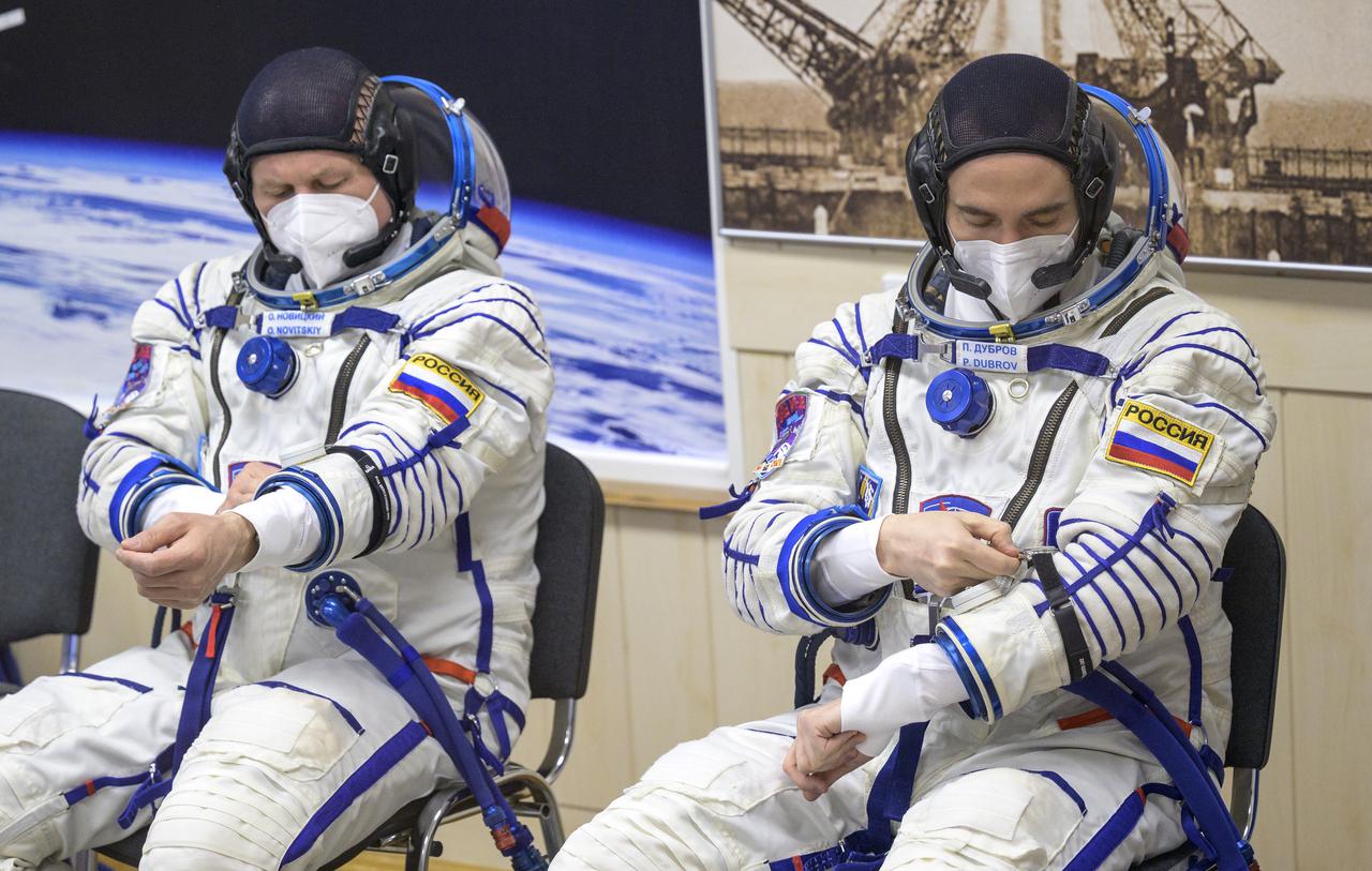 Expedition 65 Russian cosmonauts Oleg Novitskiy, left, and Pyotr Dubrov adjust their watches after donning their Russian Sokol suit as they and fellow crewmate NASA astronaut Mark Vande Hei prepare for their Soyuz launch to the International Space Station Friday, April 9, 2021 in Baikonur, Kazakhstan. Launch of the Soyuz rocket sent the trio on a mission to the International Space Station. Photo Credit: (NASA/Bill Ingalls)