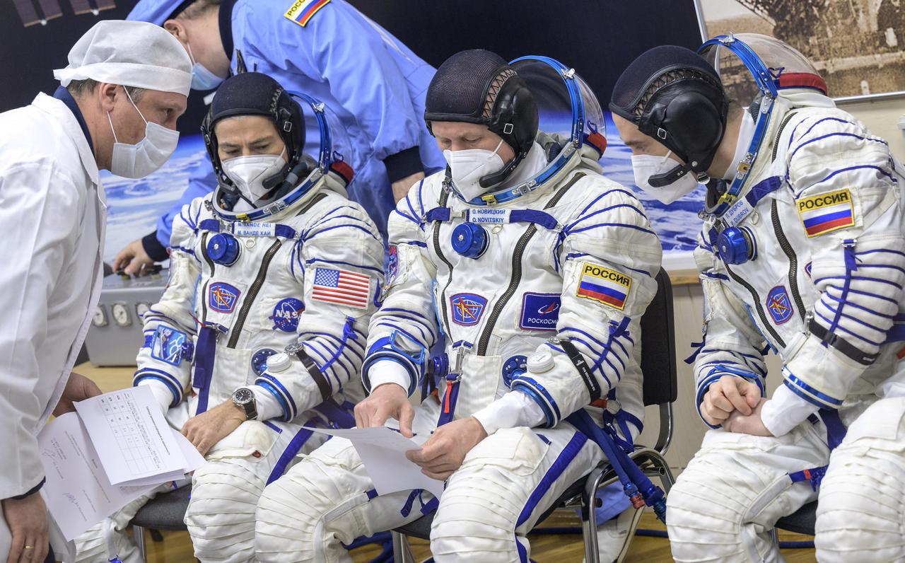 Expedition 65 NASA astronaut Mark Vande Hei, left, Russian cosmonauts Oleg Novitskiy, center, and Pyotr Dubrov talk with technicians after donning their Russian Sokol suits as they prepare for their Soyuz launch to the International Space Station Friday, April 9, 2021 in Baikonur, Kazakhstan. Launch of the Soyuz rocket sent the trio on a mission to the International Space Station. Photo Credit: (NASA/Bill Ingalls)