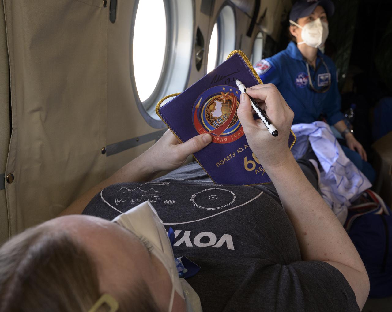Expedition 64 NASA astronaut Kate Rubins signs a memento while onboard a Russian MI-8 helicopter that will take her to Karaganda after she, and Roscosmos cosmonauts Sergey Ryzhikov and Sergey Kud-Sverchkov, landed in their Soyuz MS-17 spacecraft near the town of Zhezkazgan, Kazakhstan on Saturday, April 17, 2021. Rubins, Ryzhikov and Kud-Sverchkov returned after 185 days in space having served as Expedition 63-64 crew members onboard the International Space Station. Photo Credit: NASA/Bill Ingalls