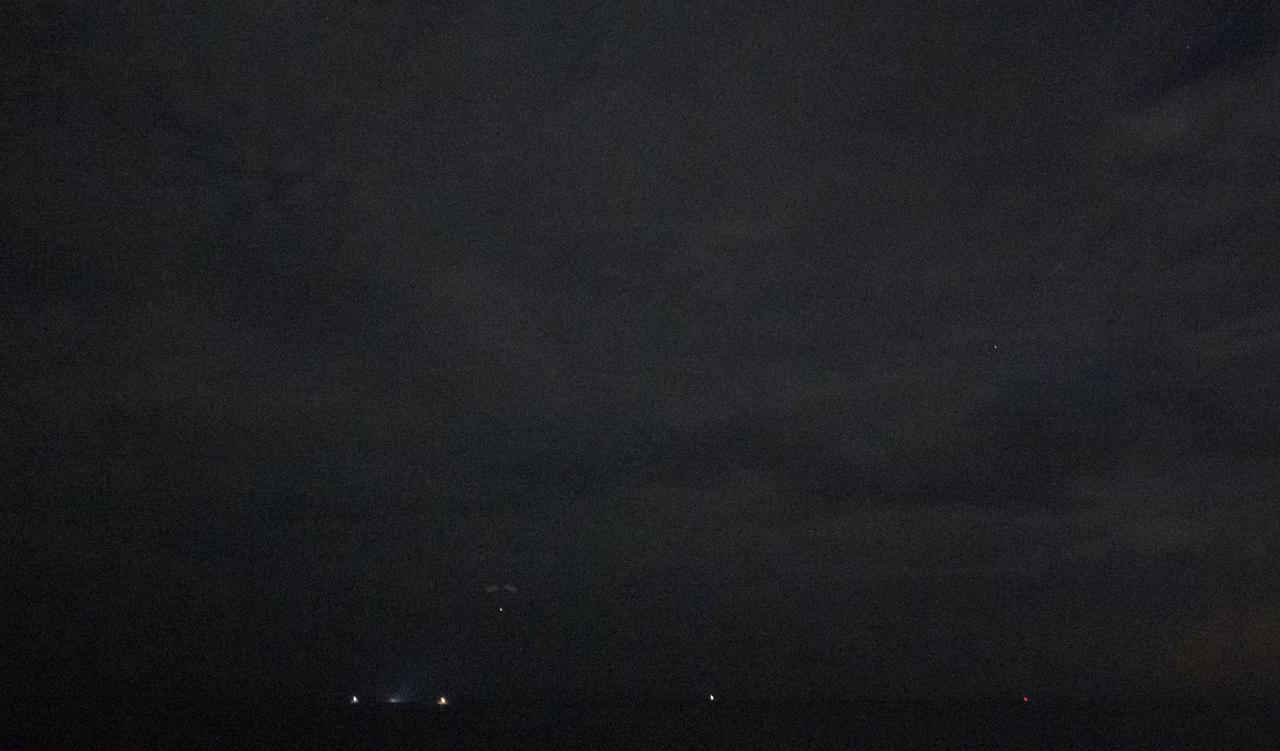 The SpaceX Crew Dragon Resilience spacecraft is seen in the distance as it lands with NASA astronauts Mike Hopkins, Shannon Walker, and Victor Glover, and Japan Aerospace Exploration Agency (JAXA) astronaut Soichi Noguchi aboard in the Gulf of Mexico off the coast of Panama City, Florida, Sunday, May 2, 2021. NASA’s SpaceX Crew-1 mission was the first crew rotation flight of the SpaceX Crew Dragon spacecraft and Falcon 9 rocket with astronauts to the International Space Station as part of the agency’s Commercial Crew Program. Note - this image noise is a result of using a very high sensitivity setting in the camera in a very dark situation. Photo Credit: (NASA/Bill Ingalls)
