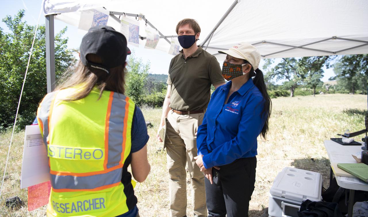 Lauren Claudatos, researcher for STEReO, the Scalable Traffic Management for Emergency Response Operations project, at NASA's Ames Research Center, right, speaks with Richard Barhydt, station director of the U.S. Forest Service's Pacific Southwest Research Station, left, and Huy Tran, director of aeronautics at NASA's Ames Research Center, center, during STEReO test activities, Tuesday, May 4, 2021 as Cal Fire conducts aerial fire fighting training exercises near Redding, California. STEReO, the Scalable Traffic Management for Emergency Response Operations project, led by NASA’s Ames Research Center, builds on NASA’s expertise in air traffic management, human factors research, and autonomous technology development to apply the agency’s work in Unmanned Aircraft Systems Traffic Management, or UTM, to public safety uses. Photo Credit: (NASA/Joel Kowsky)