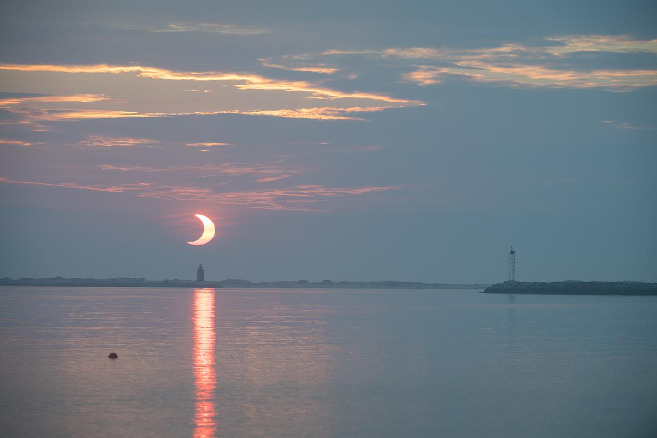 A partial solar eclipse is seen as the sun rises behind the Delaware Breakwater Lighthouse, Thursday, June 10, 2021, at Lewes Beach in Delaware. The annular or “ring of fire” solar eclipse is only visible to some parts of Greenland, Northern Russia, and Canada. Photo Credit: (NASA/Aubrey Gemignani)