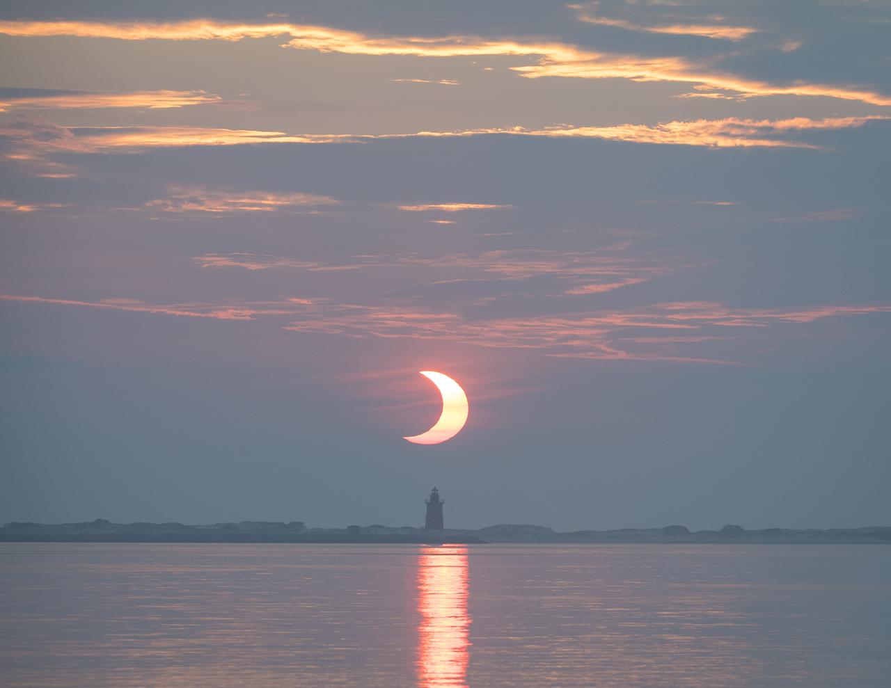 A partial solar eclipse is seen as the sun rises behind the Delaware Breakwater Lighthouse, Thursday, June 10, 2021, at Lewes Beach in Delaware. The annular or “ring of fire” solar eclipse is only visible to some parts of Greenland, Northern Russia, and Canada. Photo Credit: (NASA/Aubrey Gemignani)