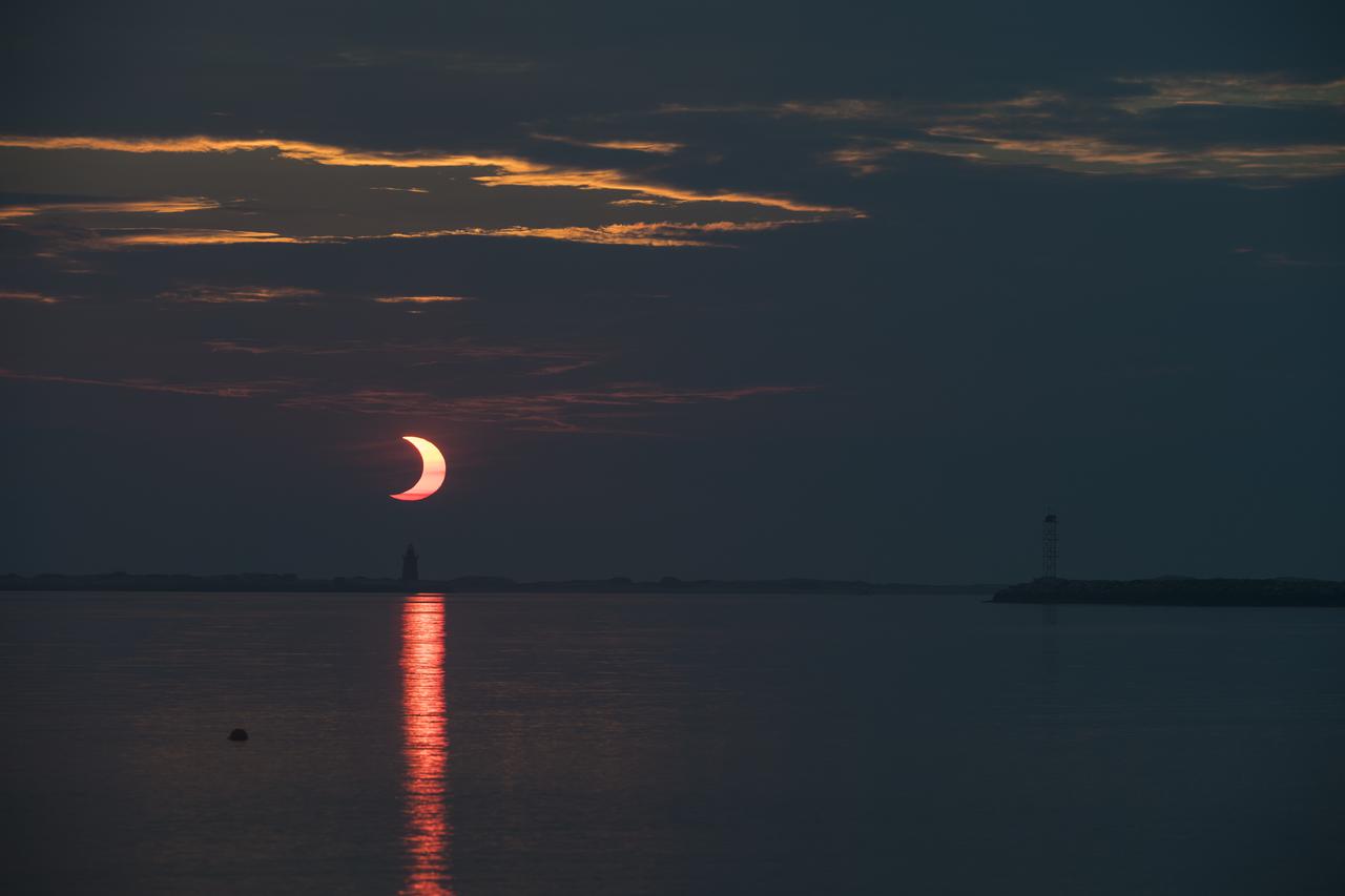 A partial solar eclipse is seen as the sun rises behind the Delaware Breakwater Lighthouse, Thursday, June 10, 2021, at Lewes Beach in Delaware. The annular or “ring of fire” solar eclipse is only visible to some parts of Greenland, Northern Russia, and Canada. Photo Credit: (NASA/Aubrey Gemignani)