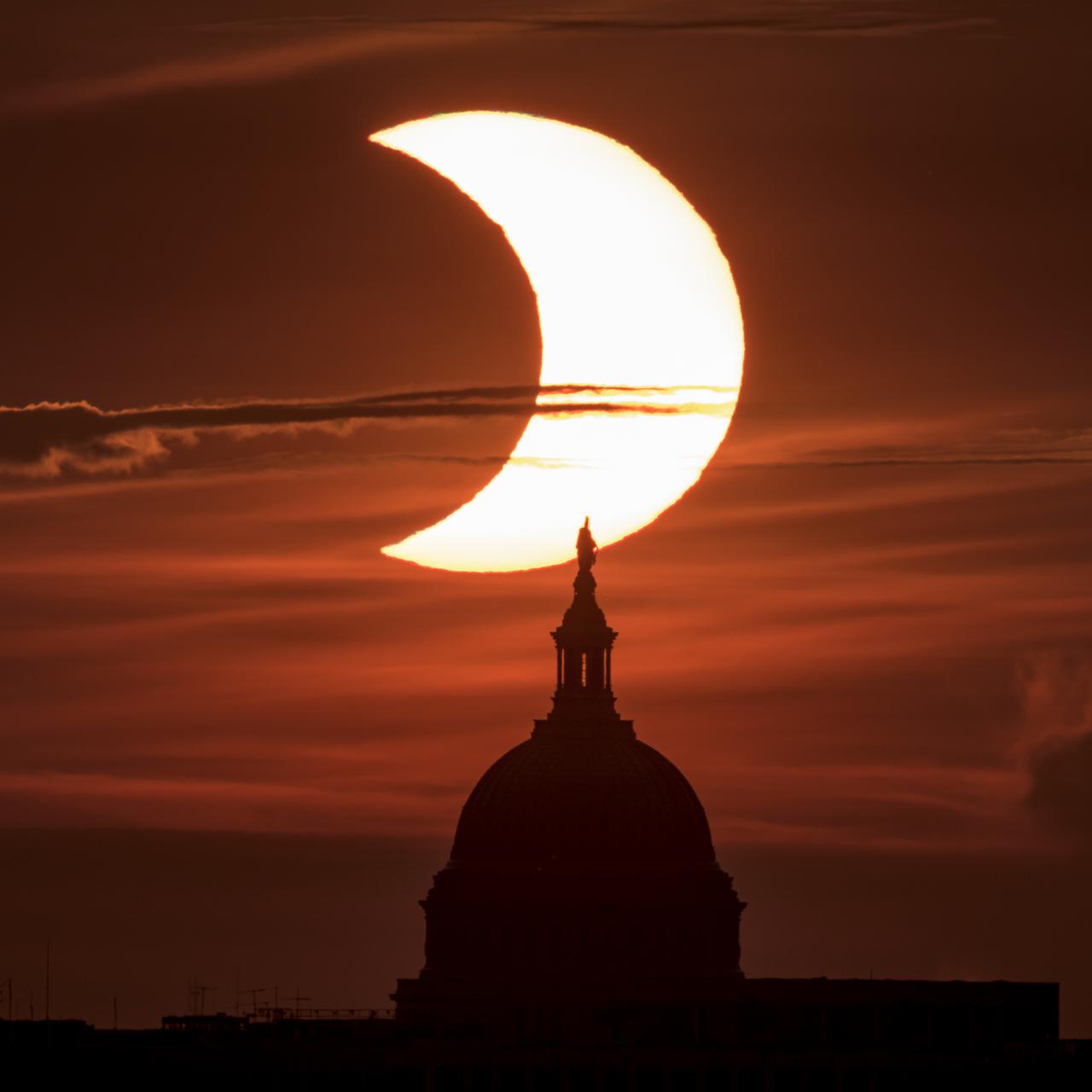 A partial solar eclipse is seen as the sun rises behind the United States Capitol Building, Thursday, June 10, 2021, as seen from Arlington, Virginia. The annular or “ring of fire” solar eclipse is only visible to some people in Greenland, Northern Russia, and Canada. Photo Credit: (NASA/Bill Ingalls)