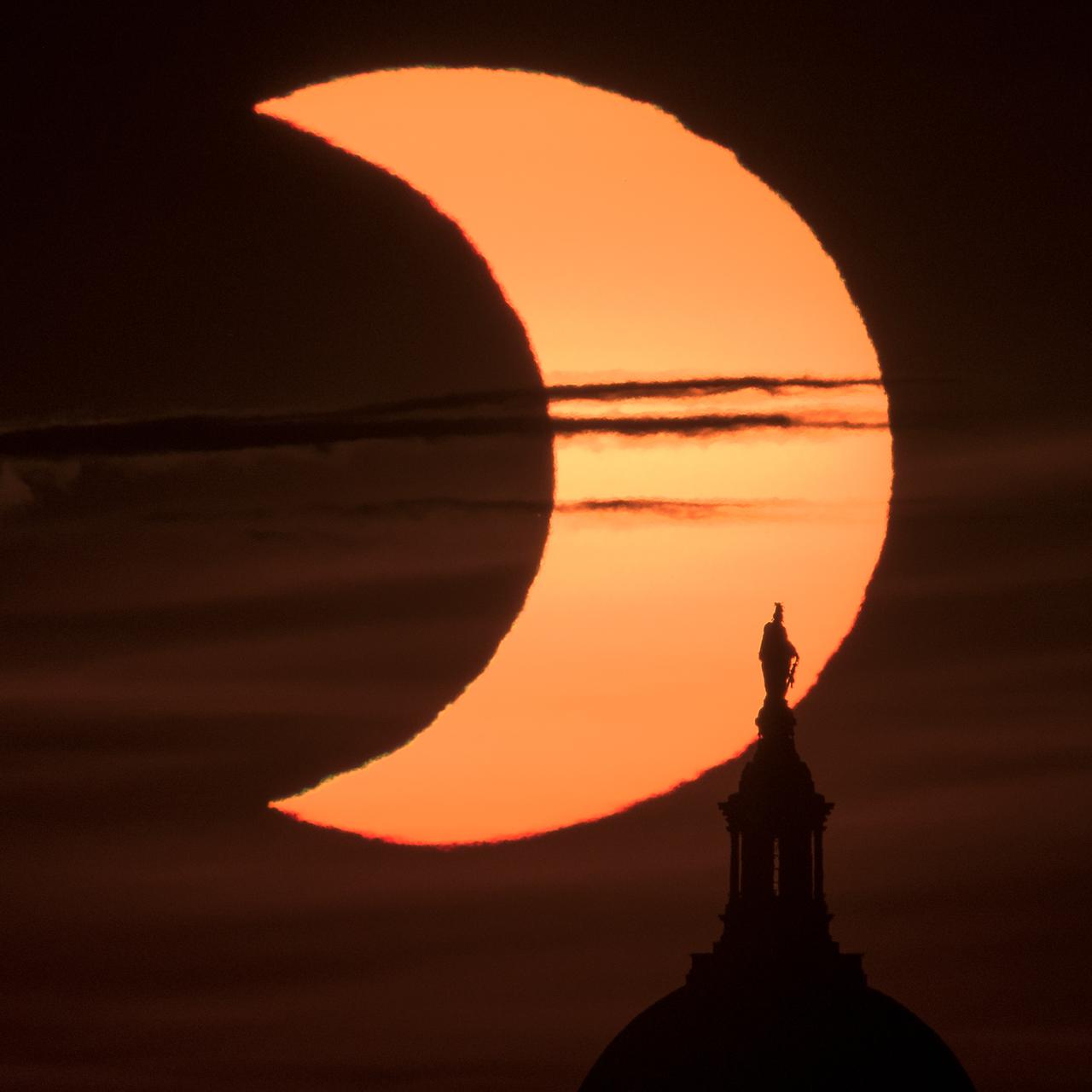 A partial solar eclipse is seen as the sun rises behind the Statue of Freedom atop the United States Capitol Building, Thursday, June 10, 2021, as seen from Arlington, Virginia. The annular or “ring of fire” solar eclipse is only visible to some people in Greenland, Northern Russia, and Canada. Photo Credit: (NASA/Bill Ingalls)