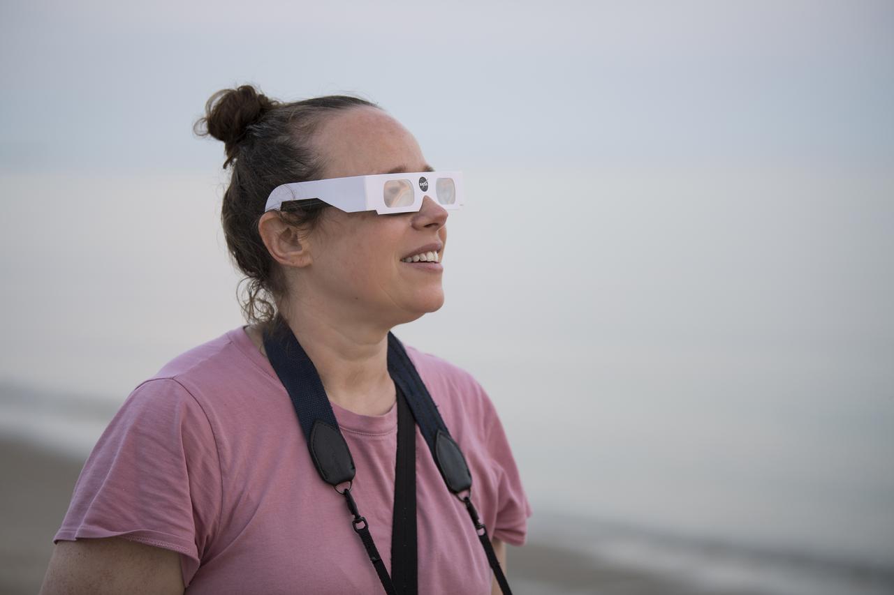 Sarah Baker views the partial solar eclipse as the sun rises, Thursday, June 10, 2021, at Lewes Beach in Delaware. The annular or “ring of fire” solar eclipse is only visible to some parts of Greenland, Northern Russia, and Canada. Photo Credit: (NASA/Aubrey Gemignani)