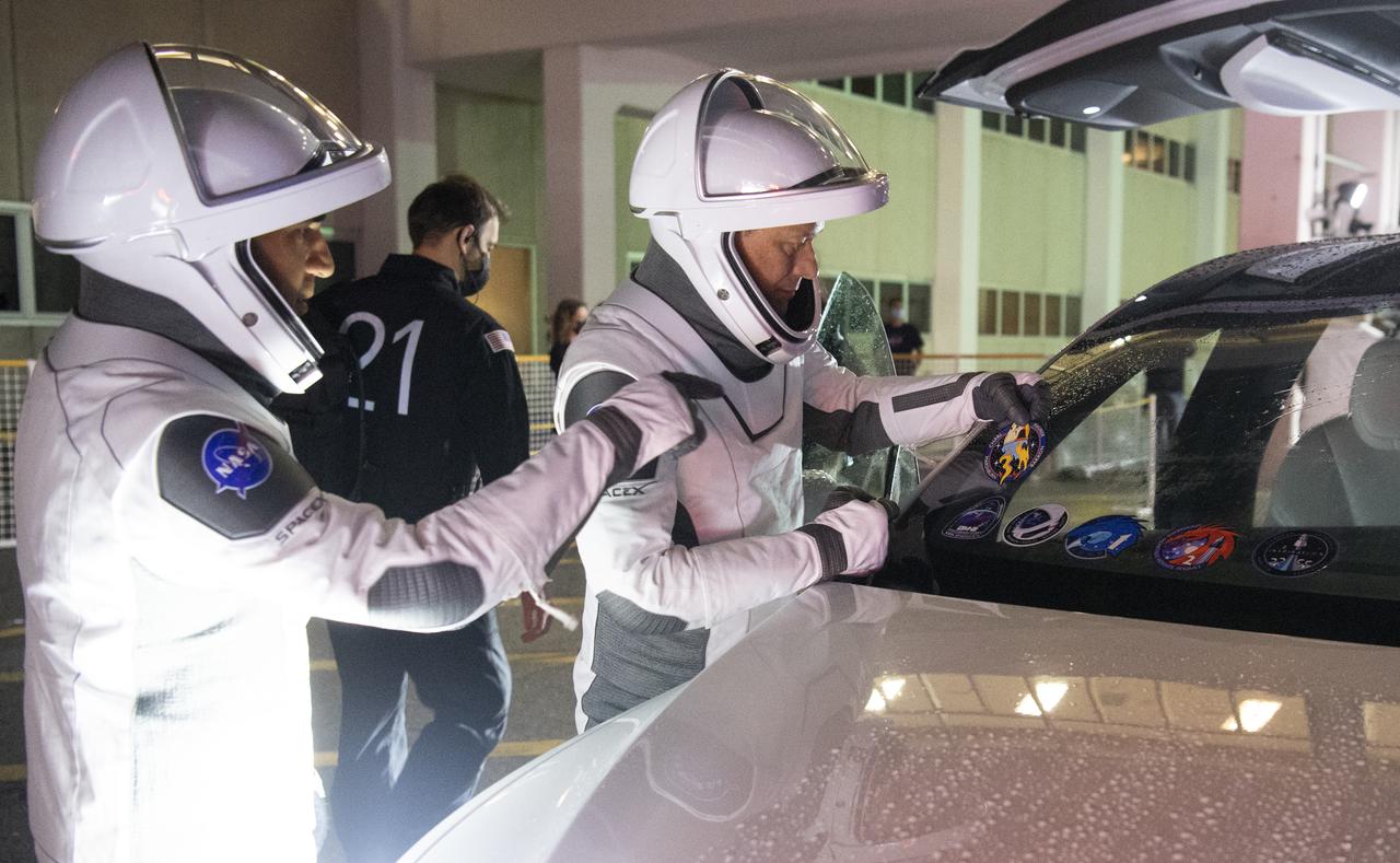 NASA astronauts Raja Chari, left, and Tom Marshburn, wearing SpaceX spacesuits, are seen as they place a sticker of the Crew-3 mission patch on the windshield of the vehicle that will take them to the launch pad as they prepare to depart the Neil A. Armstrong Operations and Checkout Building for Launch Complex 39A during a dress rehearsal prior to the Crew-3 mission launch, Thursday, Oct. 28, 2021, at NASA’s Kennedy Space Center in Florida. NASA’s SpaceX Crew-3 mission is the third crew rotation mission of the SpaceX Crew Dragon spacecraft and Falcon 9 rocket to the International Space Station as part of the agency’s Commercial Crew Program. Chari, Marshburn, Barron, Maurer are scheduled to launch at Oct. 31 at 2:21 a.m. ET, from Launch Complex 39A at the Kennedy Space Center. Photo Credit: (NASA/Joel Kowsky)