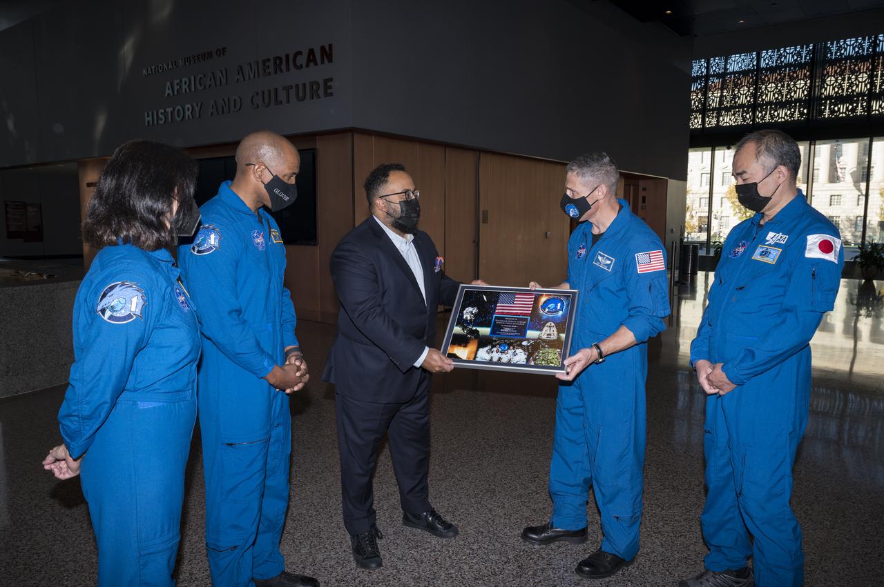 SpaceX Crew-1 NASA astronauts, Shannon Walker, left, Victor Glover, second from left, Mike Hopkins, second from right, and Japan Aerospace Exploration Agency (JAXA) astronaut Soichi Noguchi, right, present a montage from the Crew-1 mission to the director of the National Museum of African American History and Culture, Kevin Young, Tuesday, Nov. 16, 2021, in Washington. Hopkins, Glover, Walker, and Noguchi launched on the first crew rotation mission to the International Space Station for SpaceX’s Falcon 9 and Crew Dragon spacecraft as part of the agency’s Commercial Crew Program and spent 168 days in space across Expeditions 64 and 65. Photo Credit: (NASA/Aubrey Gemignani)