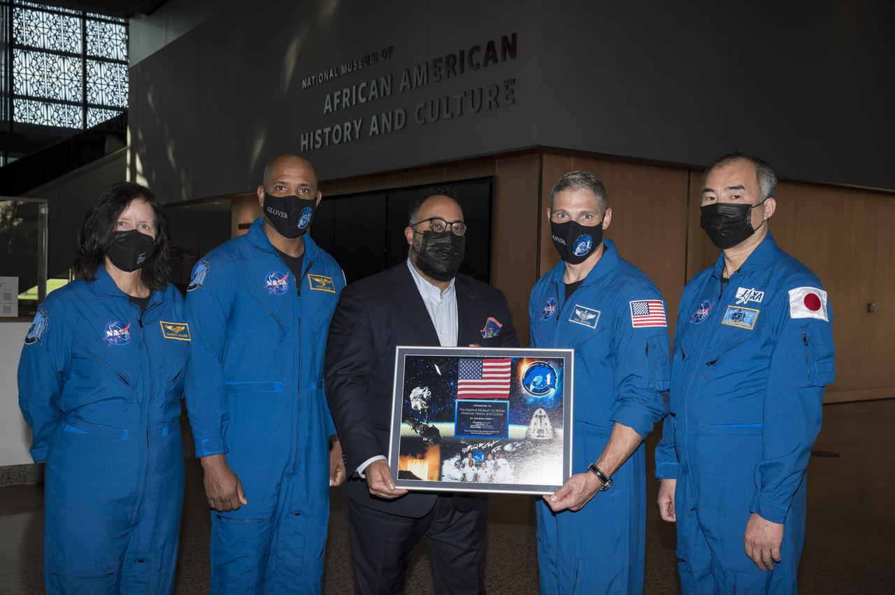 SpaceX Crew-1 NASA astronauts, Shannon Walker, left, Victor Glover, second from left, Mike Hopkins, second from right, and Japan Aerospace Exploration Agency (JAXA) astronaut Soichi Noguchi, right, present a montage from the Crew-1 mission to the director of the National Museum of African American History and Culture, Kevin Young, Tuesday, Nov. 16, 2021, in Washington. Hopkins, Glover, Walker, and Noguchi launched on the first crew rotation mission to the International Space Station for SpaceX’s Falcon 9 and Crew Dragon spacecraft as part of the agency’s Commercial Crew Program and spent 168 days in space across Expeditions 64 and 65. Photo Credit: (NASA/Aubrey Gemignani)