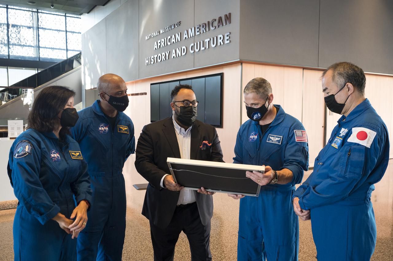 SpaceX Crew-1 NASA astronauts, Shannon Walker, left, Victor Glover, second from left, Mike Hopkins, second from right, and Japan Aerospace Exploration Agency (JAXA) astronaut Soichi Noguchi, right, present a montage from the Crew-1 mission to the director of the National Museum of African American History and Culture, Kevin Young, Tuesday, Nov. 16, 2021, in Washington. Hopkins, Glover, Walker, and Noguchi launched on the first crew rotation mission to the International Space Station for SpaceX’s Falcon 9 and Crew Dragon spacecraft as part of the agency’s Commercial Crew Program and spent 168 days in space across Expeditions 64 and 65. Photo Credit: (NASA/Aubrey Gemignani)