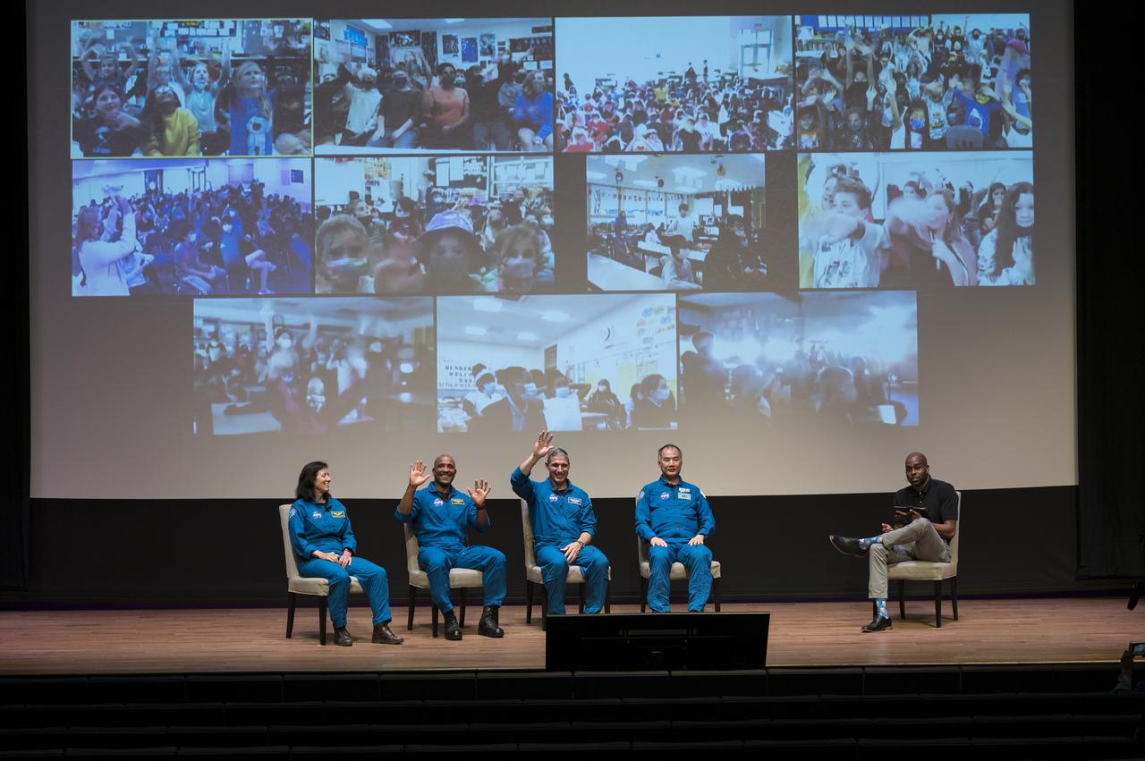 SpaceX Crew-1 NASA astronauts, from left to right, Shannon Walker, Victor Glover, Mike Hopkins, and Japan Aerospace Exploration Agency (JAXA) astronaut Soichi Noguchi, wave at students during a live question and answer session with National Museum of African American History and Culture (NMAAHC) STEM educator  Christopher Williams, right, in the Oprah Winfrey Theater at the NMAAHC, Tuesday, Nov. 16, 2021, in Washington. Hopkins, Glover, Walker, and Noguchi launched on the first crew rotation mission to the International Space Station for SpaceX’s Falcon 9 and Crew Dragon spacecraft as part of the agency’s Commercial Crew Program and spent 168 days in space across Expeditions 64 and 65. Photo Credit: (NASA/Aubrey Gemignani)