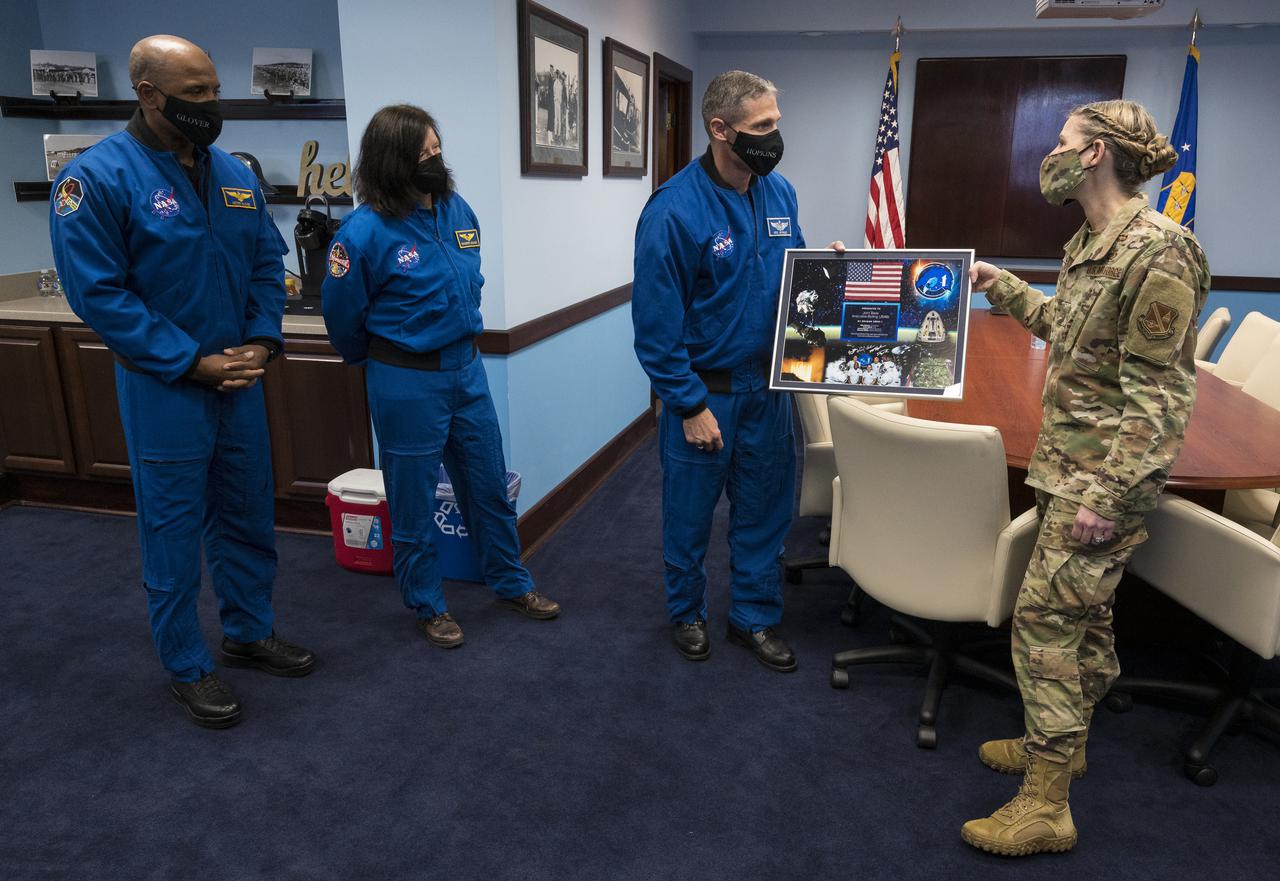 SpaceX Crew-1 NASA astronauts, from left, Victor Glover, Mike Hopkins, and Shannon Walker, present a montage from their mission to Col. Catherine Logan, commander of Joint Base Anacostia-Bolling (JBAB), Friday, Nov. 19, 2021, in Washington. Hopkins, Glover, Walker, and Japan Aerospace Exploration Agency (JAXA) astronaut Soichi Noguchi, launched on the first crew rotation mission to the International Space Station for SpaceX’s Falcon 9 and Crew Dragon spacecraft as part of the agency’s Commercial Crew Program and spent 168 days in space across Expeditions 64 and 65. Photo Credit: (NASA/Aubrey Gemignani)