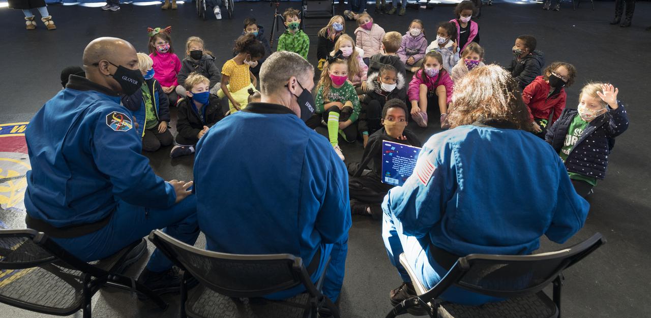 SpaceX Crew-1 NASA astronauts, from left, Victor Glover, Mike Hopkins, and Shannon Walker, read a book to students from the Learn DC public charter school at Joint Base Anacostia-Bolling (JBAB), Friday, Nov. 19, 2021, in Washington. Hopkins, Glover, Walker, and Japan Aerospace Exploration Agency (JAXA) astronaut Soichi Noguchi, launched on the first crew rotation mission to the International Space Station for SpaceX’s Falcon 9 and Crew Dragon spacecraft as part of the agency’s Commercial Crew Program and spent 168 days in space across Expeditions 64 and 65. Photo Credit: (NASA/Aubrey Gemignani)
