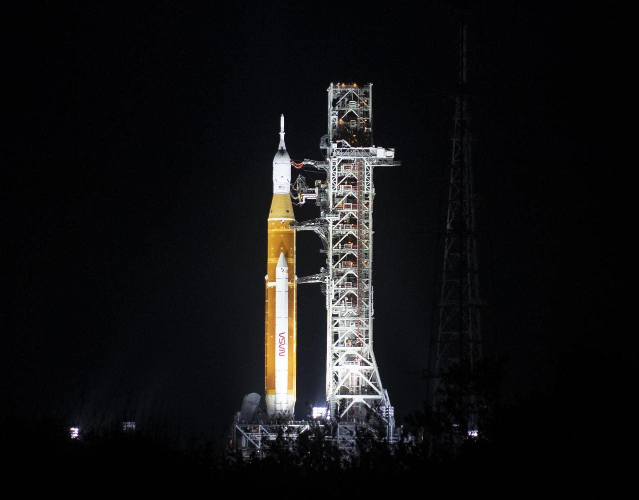 NASA’s Space Launch System (SLS) rocket with the Orion spacecraft aboard is seen illuminated by spotlights atop a mobile launcher at Launch Complex 39B, Friday, March 18, 2022, after being rollout out to the launch pad for the first time at NASA’s Kennedy Space Center in Florida. Ahead of NASA’s Artemis I flight test, the fully stacked and integrated SLS rocket and Orion spacecraft will undergo a wet dress rehearsal at Launch Complex 39B to verify systems and practice countdown procedures for the first launch. Photo Credit: (NASA/Joel Kowsky)