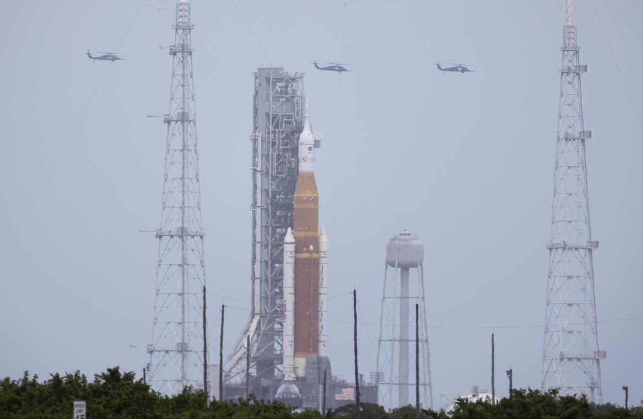 Three helicopters are seen flying past NASA’s Space Launch System (SLS) rocket with the Orion spacecraft aboard atop a mobile launcher at Launch Complex 39B, Thursday, April 21, 2022, at NASA’s Kennedy Space Center in Florida. Photo Credit: (NASA/Joel Kowsky)