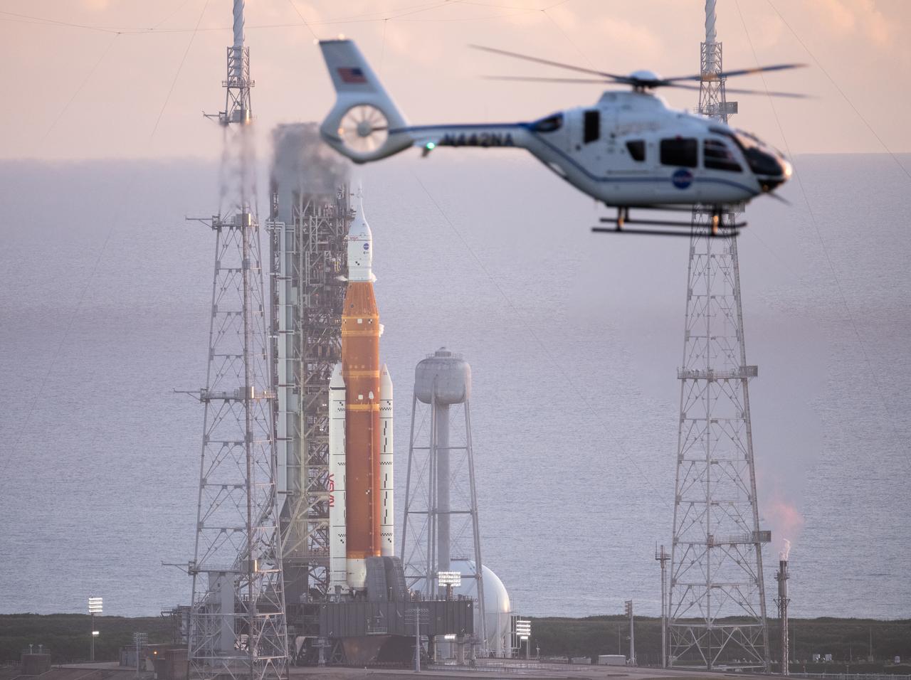 A NASA helicopter flies past the agency’s Space Launch System (SLS) rocket with the Orion spacecraft aboard atop the mobile launcher at Launch Pad 39B, Monday, Aug. 29, 2022, as the launch countdown progresses at NASA’s Kennedy Space Center in Florida. NASA’s Artemis I flight test is the first integrated test of the agency’s deep space exploration systems: the Orion spacecraft, SLS rocket, and supporting ground systems. The launch director halted today’s launch attempt at approximately 8:30 a.m. ET.  Photo Credit: (NASA/Joel Kowsky)