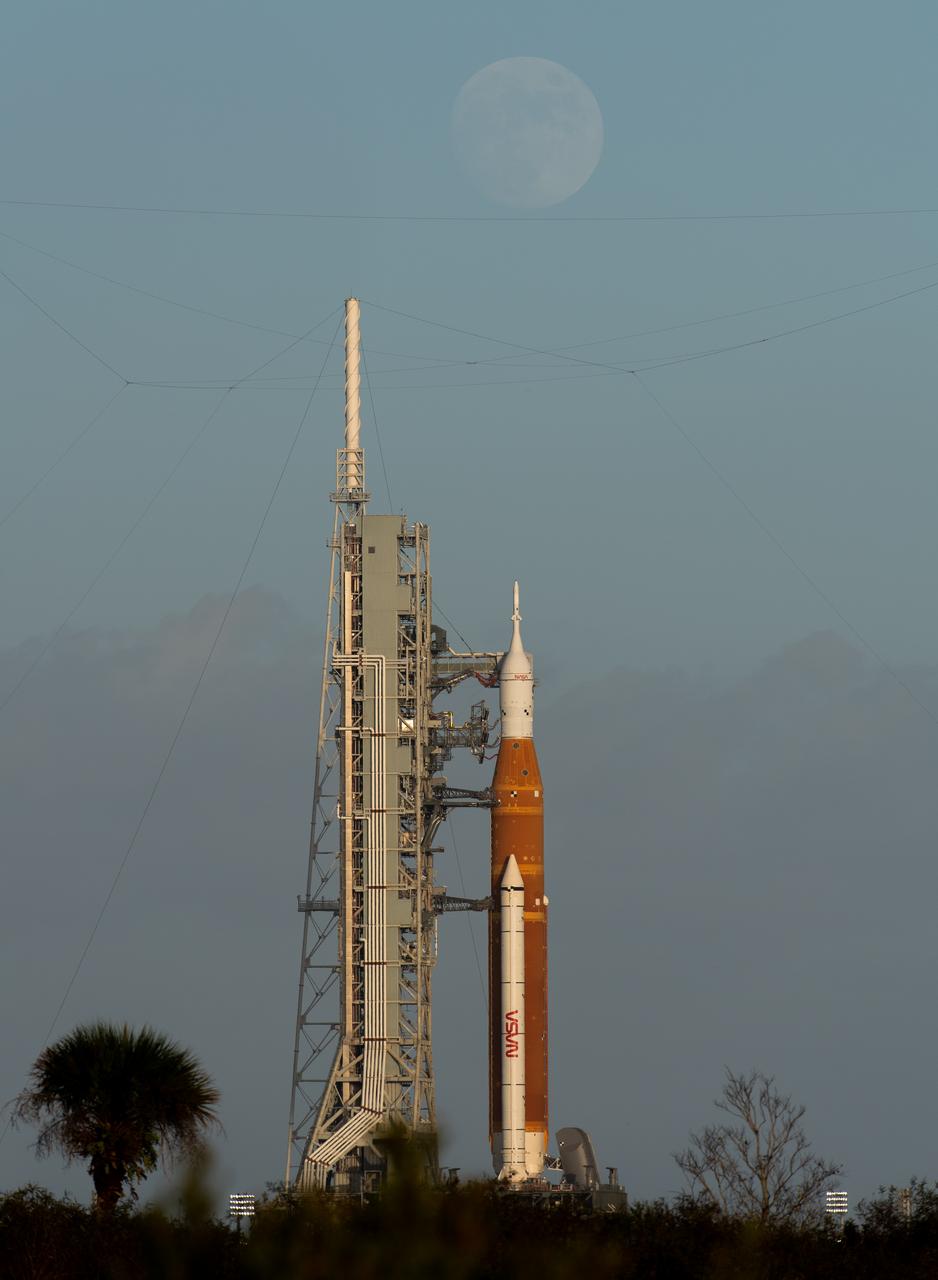 The Moon is seen as it rises behind NASA’s Space Launch System (SLS) rocket with the Orion spacecraft aboard atop the mobile launcher at Launch Pad 39B as preparations for launch continue, Sunday, Nov. 6, 2022, at NASA’s Kennedy Space Center in Florida. NASA’s Artemis I flight test is the first integrated test of the agency’s deep space exploration systems: the Orion spacecraft, SLS rocket, and supporting ground systems. Launch of the uncrewed flight test is targeted for Nov. 14 at 12:07 a.m. EST. Photo Credit: (NASA/Joel Kowsky)