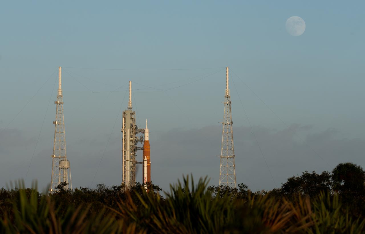 The Moon is seen as it rises behind NASA’s Space Launch System (SLS) rocket with the Orion spacecraft aboard atop the mobile launcher at Launch Pad 39B as preparations for launch continue, Sunday, Nov. 6, 2022, at NASA’s Kennedy Space Center in Florida. NASA’s Artemis I flight test is the first integrated test of the agency’s deep space exploration systems: the Orion spacecraft, SLS rocket, and supporting ground systems. Launch of the uncrewed flight test is targeted for Nov. 14 at 12:07 a.m. EST. Photo Credit: (NASA/Joel Kowsky)