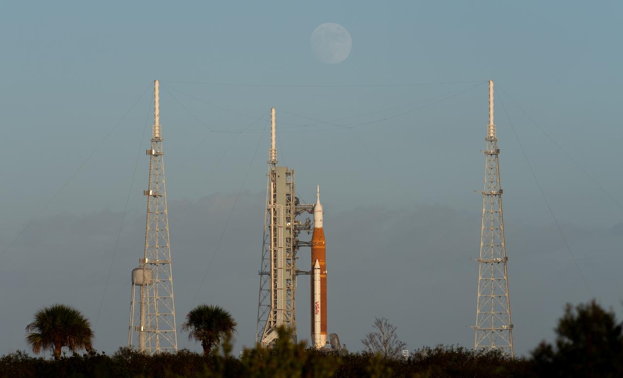 The Moon is seen as it rises behind NASA’s Space Launch System (SLS) rocket with the Orion spacecraft aboard atop the mobile launcher at Launch Pad 39B as preparations for launch continue, Sunday, Nov. 6, 2022, at NASA’s Kennedy Space Center in Florida. NASA’s Artemis I flight test is the first integrated test of the agency’s deep space exploration systems: the Orion spacecraft, SLS rocket, and supporting ground systems. Launch of the uncrewed flight test is targeted for Nov. 14 at 12:07 a.m. EST. Photo Credit: (NASA/Joel Kowsky)