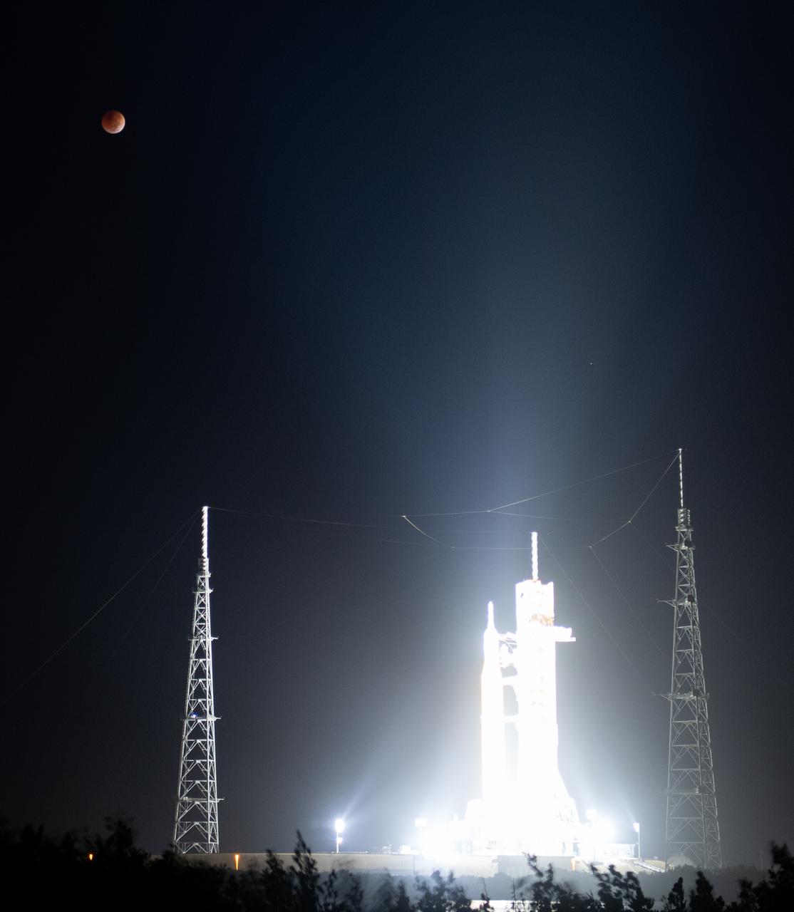 The Moon is seen during a total lunar eclipse above NASA’s Space Launch System (SLS) rocket with the Orion spacecraft aboard atop a mobile launcher at Launch Pad 39B, Tuesday, Nov. 8, 2022, at NASA’s Kennedy Space Center in Florida. NASA’s Artemis I flight test is the first integrated test of the agency’s deep space exploration systems: the Orion spacecraft, SLS rocket, and supporting ground systems. Photo Credit: (NASA/Joel Kowsky)