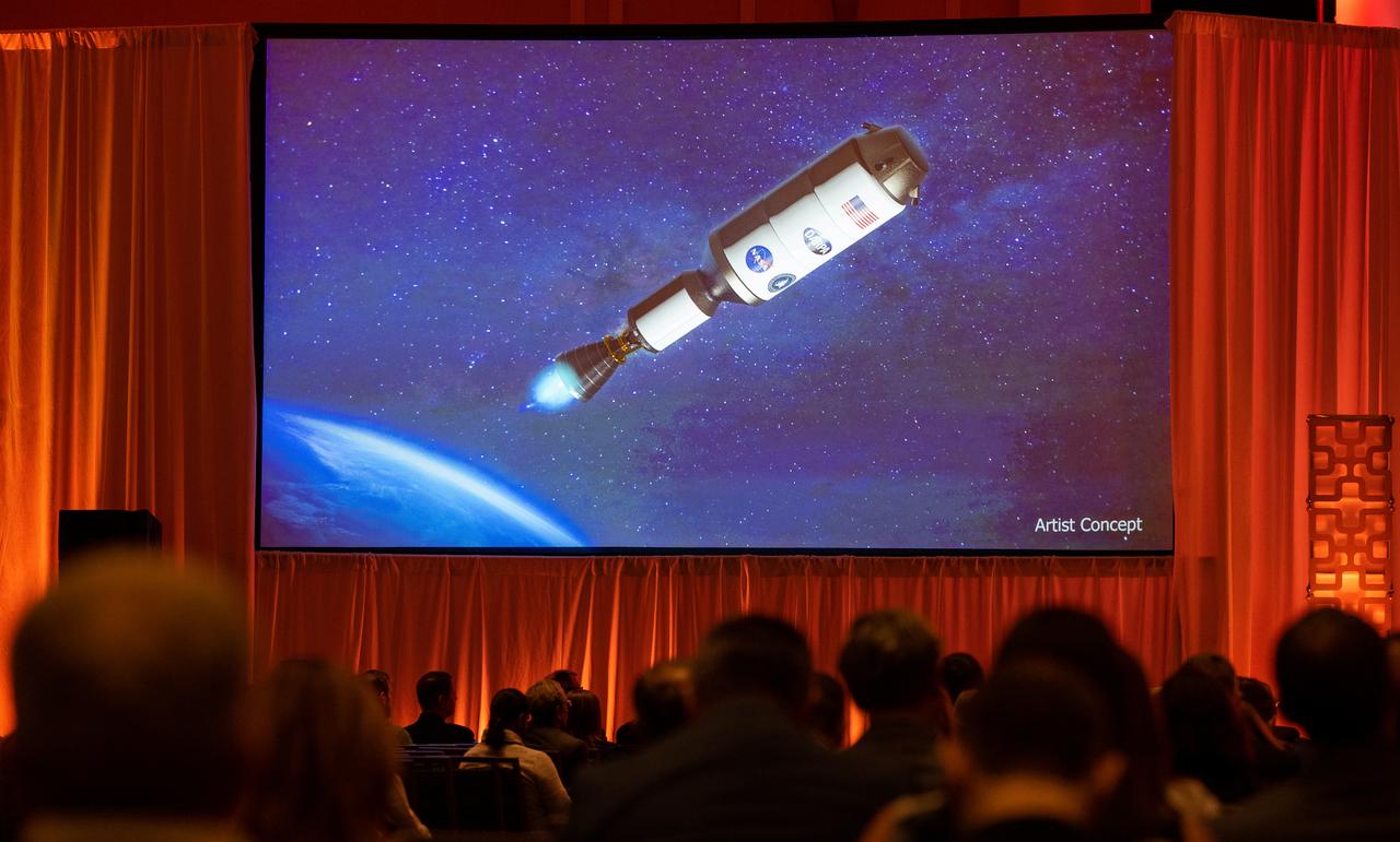 An artists concept of the Demonstration Rocket for Agile Cislunar Operations, or DRACO, spacecraft is seen on a screen during a fireside chat announcing a new collaboration on nuclear thermal propulsion at the American Institute of Aeronautics and Astronautics SciTech Forum, Tuesday, Jan. 24, 2023, at the Gaylord National Resort and Convention Center in National Harbor, Md. NASA and the Defense Advanced Research Projects Agency (DARPA) will partner on the Demonstration Rocket for Agile Cislunar Operations, or DRACO, project to develop and demonstrate in-space a nuclear thermal engine. Photo Credit: (NASA/Joel Kowsky)