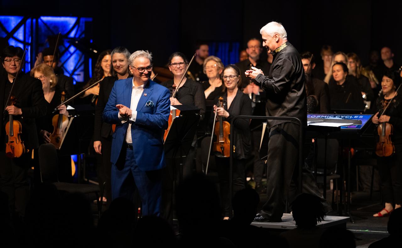 Composer Henry Dehlinger, left, and Maestro Piotr Gajewski, right, are seen with the National Philharmonic following the world premier performance of Dehlinger’s “Cosmic Cycles,” Thursday, May 11, 2023, at Capital One Hall in Tysons, Va. “Cosmic Cycles: A Space Symphony” is a collaboration between composer Henry Dehlinger, NASA’s Goddard Space Flight Center, and the National Philharmonic that features a fusion of music and video in seven multimedia works on the Sun, Earth, Moon, Planets, and Cosmos.  Photo Credit: (NASA/Joel Kowsky)