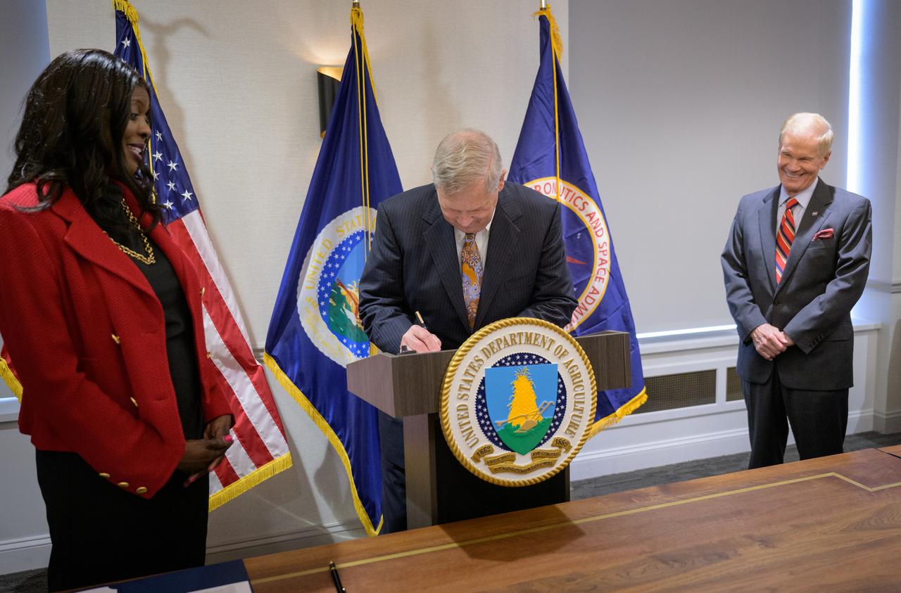 U.S. Secretary of Agriculture Thomas Vilsack signs a memorandum of understanding between NASA and USDA as Undersecretary of Agriculture for research, education and economics, Chavonda Jacobs-Young, left, and NASA Administrator Bill Nelson, look on, Wednesday, June 21, 2023, at the USDA’s Jamie L. Whitten Building in Washington. The agreement strengthens the collaboration between the two agencies, including efforts to improve agricultural and Earth science research, technology, and agricultural management, as well as the application of science data and models to agricultural decision making. Photo Credit: (NASA/Bill Ingalls)