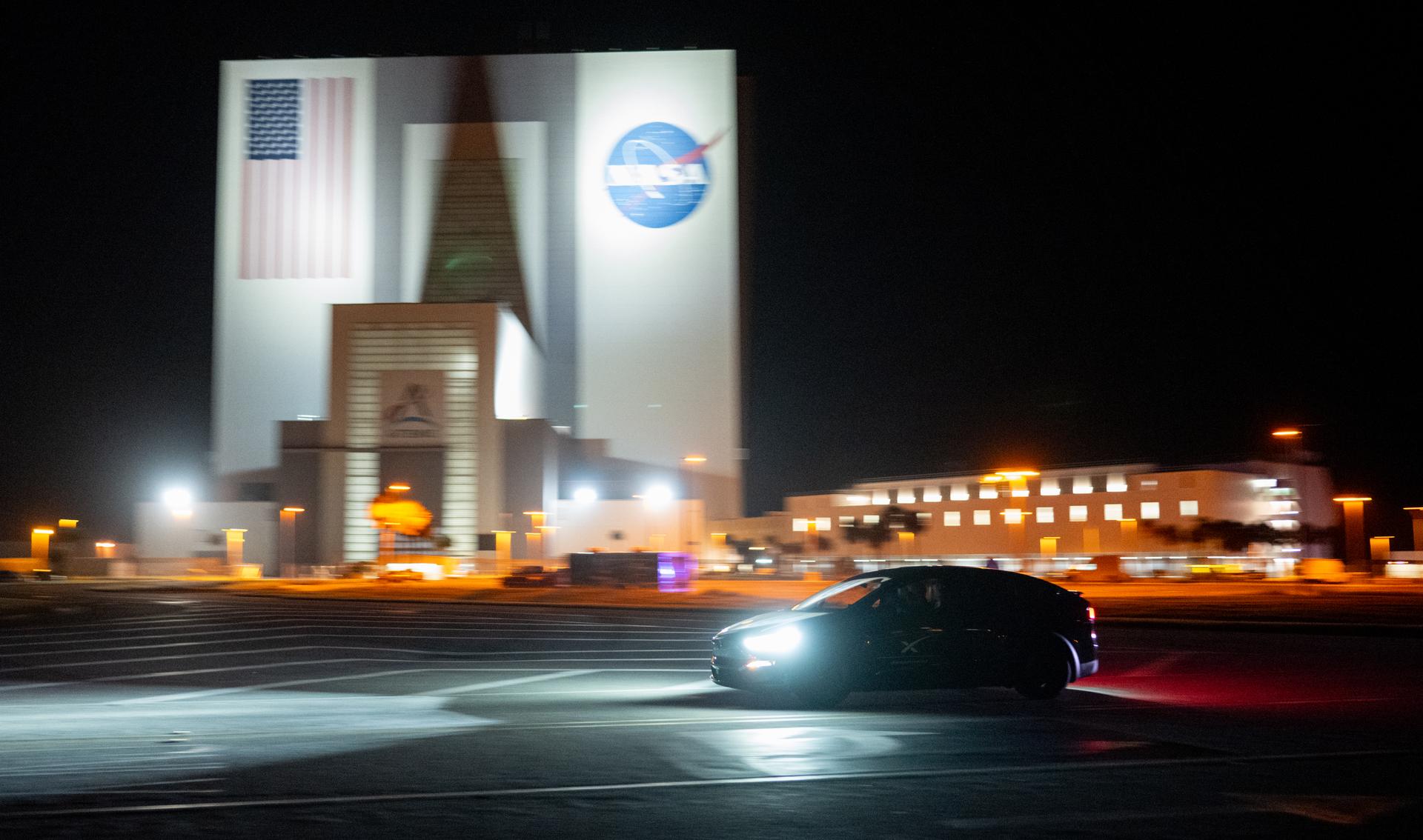 A vehicle carrying two members of NASA’s SpaceX Crew-7 mission passes by the Vehicle Assembly Building.