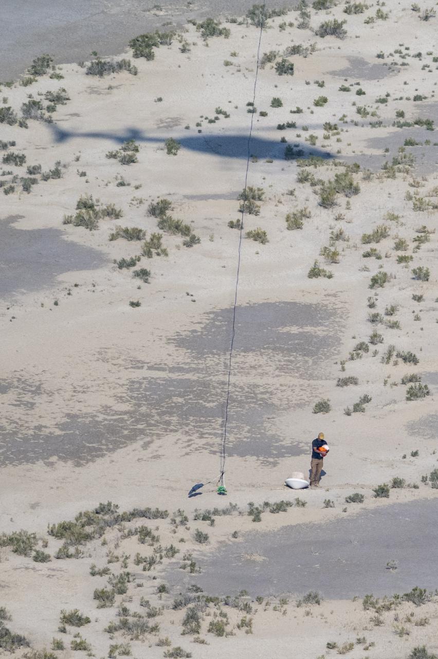 A recovery team member is seen with the training model of the sample return capsule following a drop test in preparation for the retrieval of the sample return capsule from NASA's OSIRIS-REx mission, Wednesday, Aug. 30, 2023, at the Department of Defense's Utah Test and Training Range. The sample was collected from asteroid Bennu in October 2020 by NASA’s OSIRIS-REx spacecraft and will return to Earth on September 24th, landing under parachute at the Utah Test and Training Range. Photo Credit: (NASA/Keegan Barber)