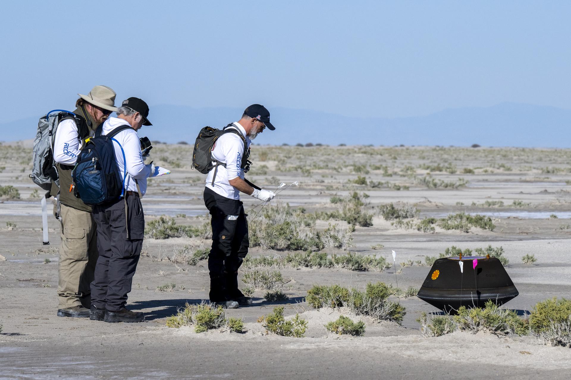 Three men look at the OSIRIS-REx sample capsule in the desert.