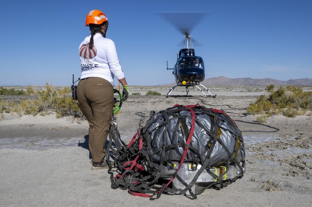On Scene Commander of Recovery Jasmine Nakayama attaches the sample return capsule from NASA’s OSIRIS-REx mission to a helicopter for transport to the cleanroom, Sunday, Sept. 24, 2023, shortly after the capsule landed at the Department of Defense's Utah Test and Training Range. The sample was collected from the asteroid Bennu in October 2020 by NASA’s OSIRIS-REx spacecraft. Photo Credit: (NASA/Keegan Barber