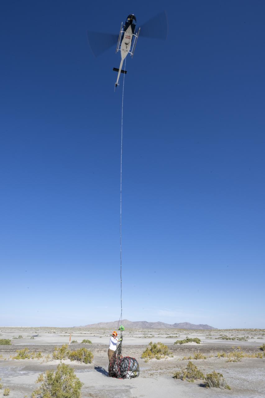 On Scene Commander of Recovery Jasmine Nakayama attaches the sample return capsule from NASA’s OSIRIS-REx mission to a helicopter for transport to the cleanroom, Sunday, Sept. 24, 2023, shortly after the capsule landed at the Department of Defense's Utah Test and Training Range. The sample was collected from the asteroid Bennu in October 2020 by NASA’s OSIRIS-REx spacecraft. Photo Credit: (NASA/Keegan Barber