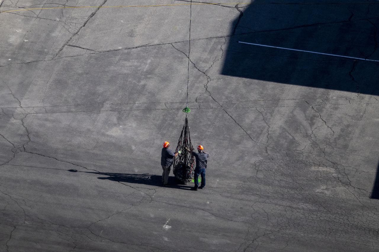 The sample return capsule from NASA’s OSIRIS-REx mission is lowered into the parking lot in front of the cleanroom hangar by helicopter, Sunday, Sept. 24, 2023, shortly after the capsule landed at the Department of Defense's Utah Test and Training Range. The sample was collected from the asteroid Bennu in October 2020 by NASA’s OSIRIS-REx spacecraft. Photo Credit: (NASA/Keegan Barber)