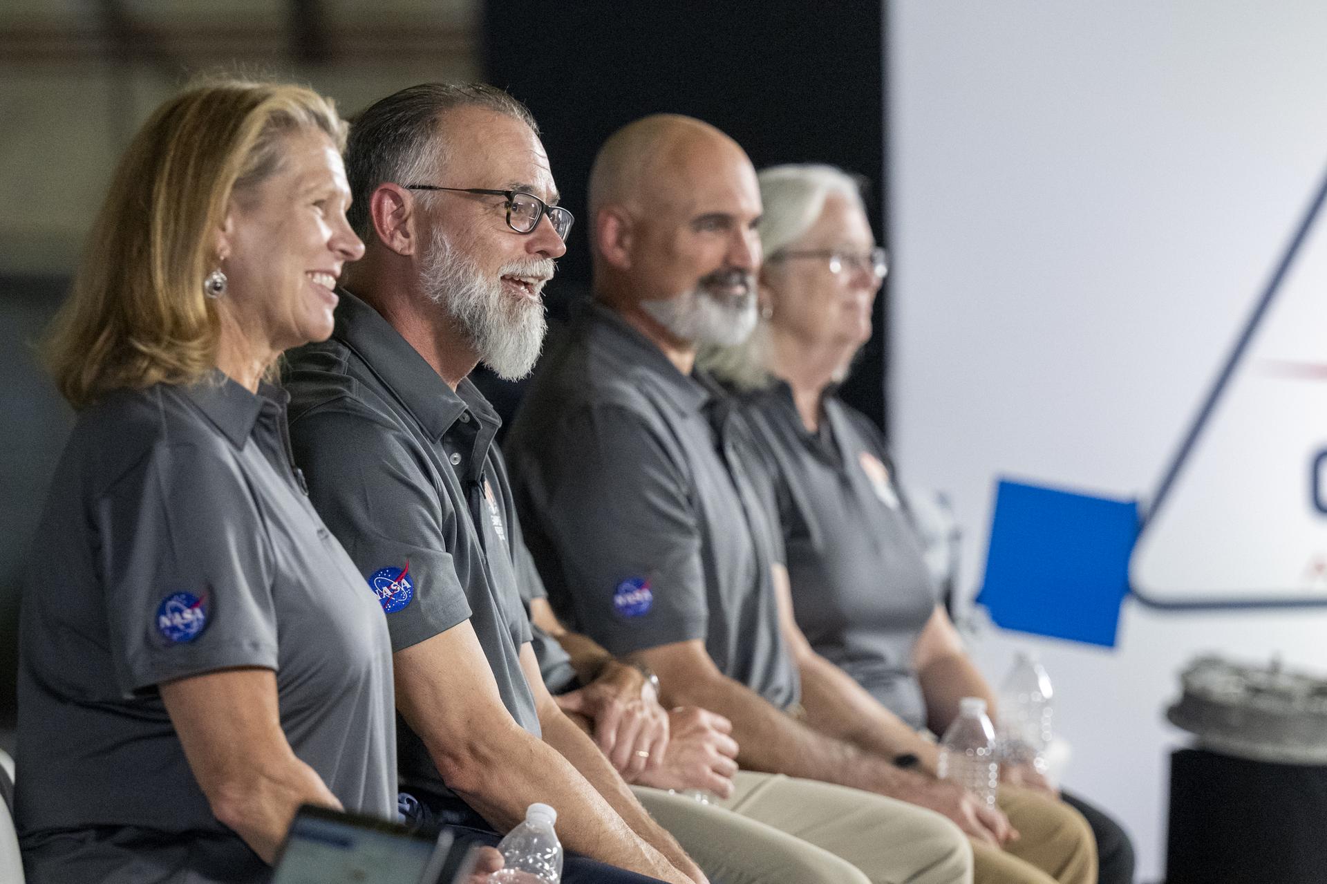 A line of people sitting and smiling. They are wearing matching gray OSIRIS-REx polos.