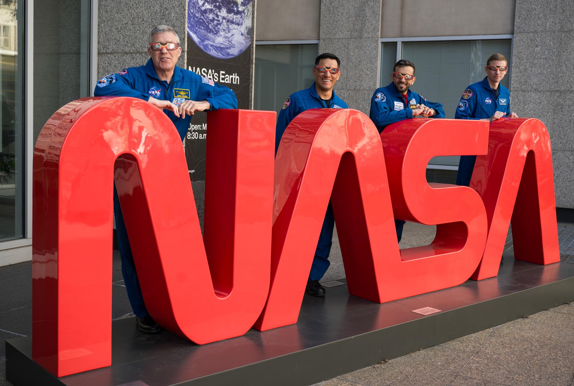 NASA astronauts Stephen Bowen, left, and Frank Rubio, UAE (United Arab Emirates) astronaut Sultan Alneyadi, and NASA astronaut Warren Hoburg, right, pose for a photo while leaning on a large, red NASA worm logo sculpture while wearing solar glasses, Tuesday, March 19, 2024, at the Mary W. Jackson NASA Headquarters building in Washington.