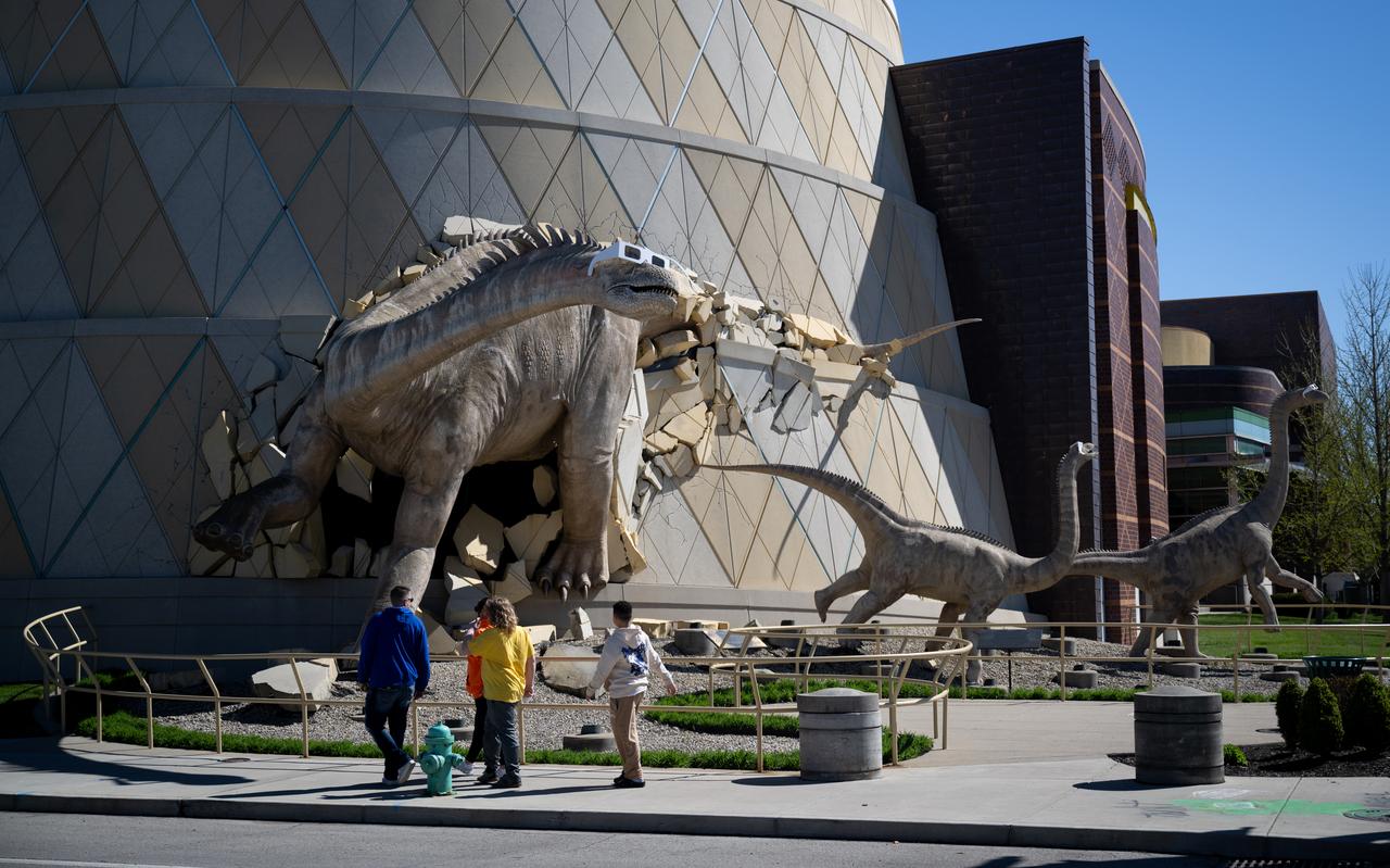 Visitors walk past sculptures of an adult and two juvenile Alamosaurs wearing solar glasses outside of The Children’s Museum of Indianapolis, Saturday, April 6, 2024, in Indianapolis, Ind. On Monday, April 8, a total solar eclipse will sweep across a narrow portion of the North American continent from Mexico’s Pacific coast to the Atlantic coast of Newfoundland, Canada, while a partial solar eclipse will be visible across the entire North American continent along with parts of Central America and Europe. Photo Credit: (NASA/Joel Kowsky)