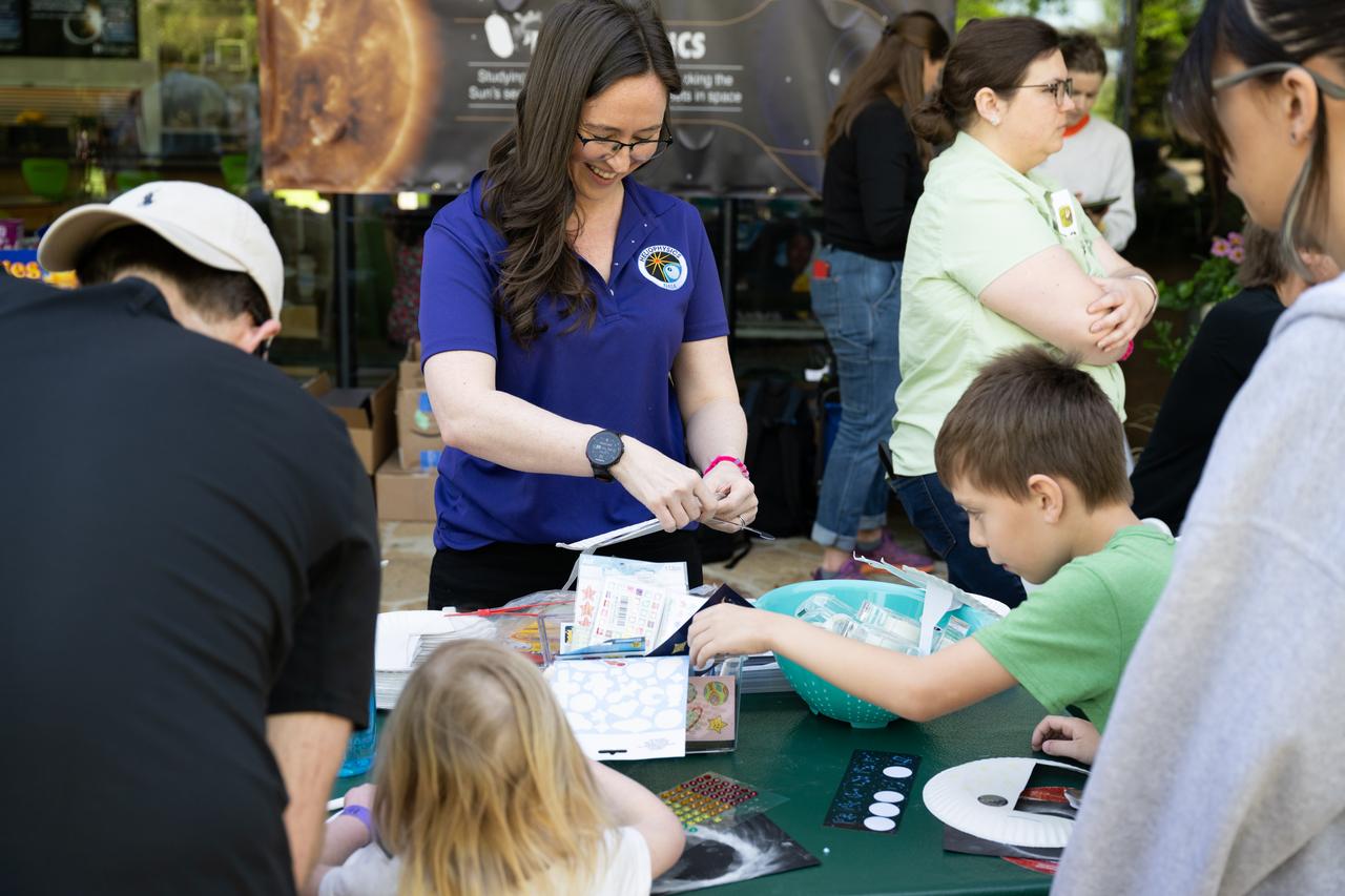 NASA Heliophysics Laboratory Research Scientist Ashley Greeley, center, works with guests at the solar eclipse glasses crafting station at the Dallas Arboretum, Sunday, April 7, 2024, in Dallas, Texas. On Monday, April 8, a total solar eclipse will sweep across a narrow portion of the North American continent from Mexico’s Pacific coast to the Atlantic coast of Newfoundland, Canada, while a partial solar eclipse will be visible across the entire North American continent along with parts of Central America and Europe. Photo Credit: (NASA/Keegan Barber)