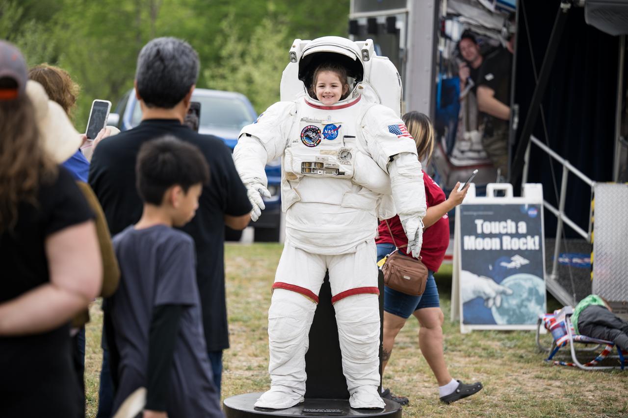 People are seen posing for photos behind a spacesuit as they prepare to watch a total solar eclipse in Kerrville, TX on Monday, April 8, 2024. A total solar eclipse swept across a narrow portion of the North American continent from Mexico’s Pacific coast to the Atlantic coast of Newfoundland, Canada. A partial solar eclipse was visible across the entire North American continent along with parts of Central America and Europe.  Photo Credit: (NASA/Aubrey Gemignani)