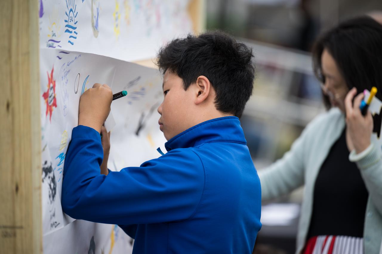 People are seen drawing on a mural as they prepare to watch a total solar eclipse in Kerrville, TX on Monday, April 8, 2024. A total solar eclipse swept across a narrow portion of the North American continent from Mexico’s Pacific coast to the Atlantic coast of Newfoundland, Canada. A partial solar eclipse was visible across the entire North American continent along with parts of Central America and Europe.  Photo Credit: (NASA/Aubrey Gemignani)