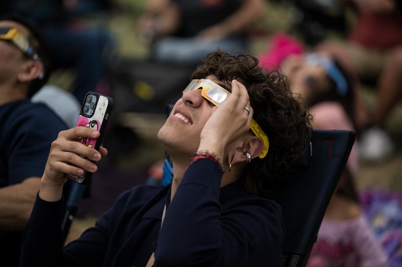 People are seen as they watch a total solar eclipse through protective glasses in Kerrville, TX on Monday, April 8, 2024. A total solar eclipse swept across a narrow portion of the North American continent from Mexico’s Pacific coast to the Atlantic coast of Newfoundland, Canada. A partial solar eclipse was visible across the entire North American continent along with parts of Central America and Europe.  Photo Credit: (NASA/Aubrey Gemignani)