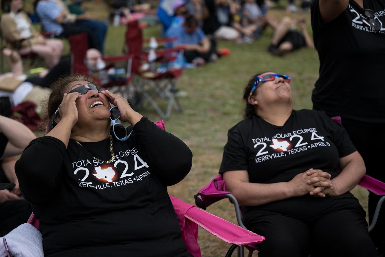 People are seen as they watch a total solar eclipse through protective glasses in Kerrville, TX on Monday, April 8, 2024. A total solar eclipse swept across a narrow portion of the North American continent from Mexico’s Pacific coast to the Atlantic coast of Newfoundland, Canada. A partial solar eclipse was visible across the entire North American continent along with parts of Central America and Europe.  Photo Credit: (NASA/Aubrey Gemignani)
