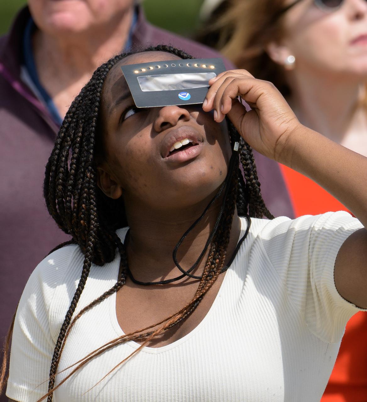 A woman watches a partial solar eclipse through protective glasses in Washington, on Monday, April 8, 2024. A total solar eclipse swept across a narrow portion of the North American continent from Mexico’s Pacific coast to the Atlantic coast of Newfoundland, Canada. A partial solar eclipse was visible across the entire North American continent along with parts of Central America and Europe.  Photo Credit: (NASA/Bill Ingalls)