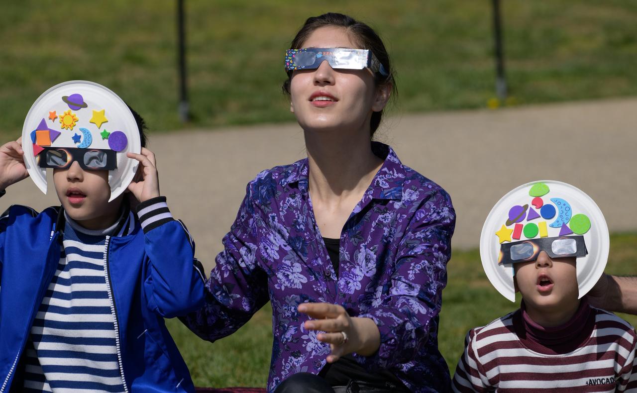 People are seen as they watch a partial solar eclipse through protective glasses in Washington, on Monday, April 8, 2024. A total solar eclipse swept across a narrow portion of the North American continent from Mexico’s Pacific coast to the Atlantic coast of Newfoundland, Canada. A partial solar eclipse was visible across the entire North American continent along with parts of Central America and Europe.  Photo Credit: (NASA/Bill Ingalls)
