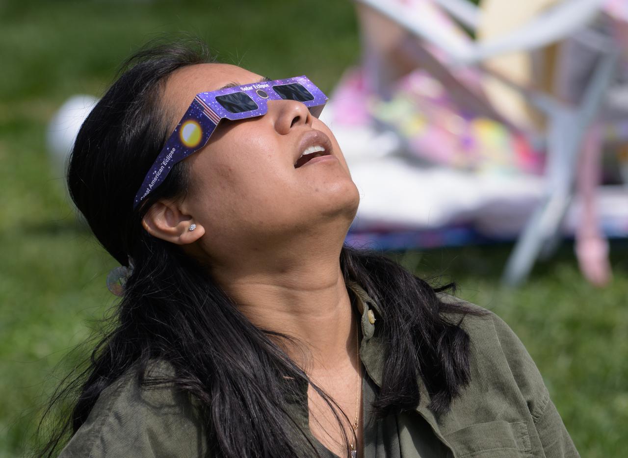 A woman watches a partial solar eclipse through protective glasses in Washington, on Monday, April 8, 2024. A total solar eclipse swept across a narrow portion of the North American continent from Mexico’s Pacific coast to the Atlantic coast of Newfoundland, Canada. A partial solar eclipse was visible across the entire North American continent along with parts of Central America and Europe.  Photo Credit: (NASA/Bill Ingalls)