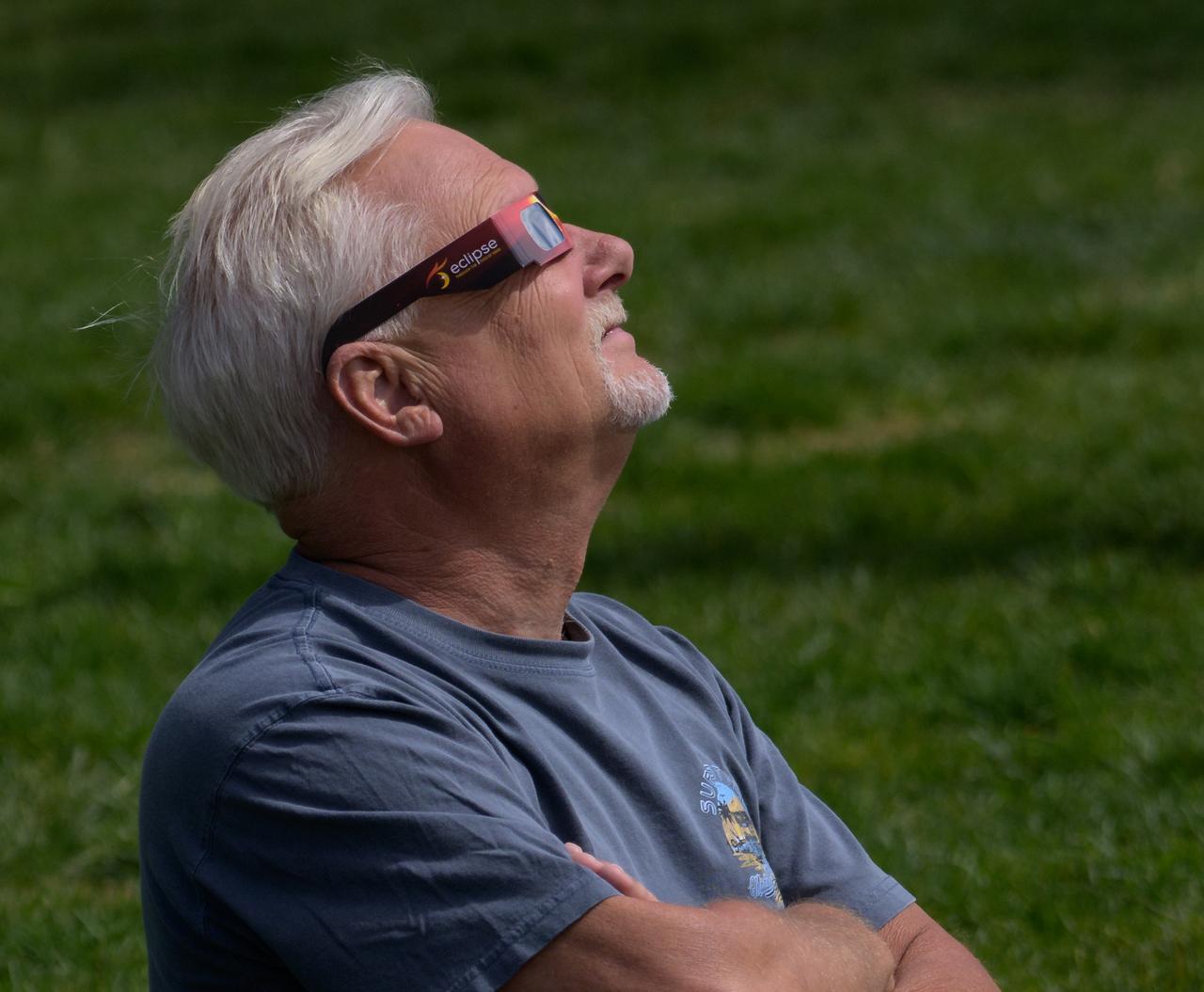 A man watches a partial solar eclipse through protective glasses in Washington, on Monday, April 8, 2024. A total solar eclipse swept across a narrow portion of the North American continent from Mexico’s Pacific coast to the Atlantic coast of Newfoundland, Canada. A partial solar eclipse was visible across the entire North American continent along with parts of Central America and Europe.  Photo Credit: (NASA/Bill Ingalls)