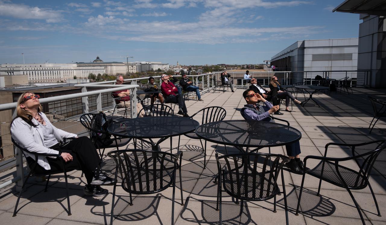 People gather on the roof of NASA Headquarters in Washington to watch a partial solar eclipse through protective glasses in Washington, on Monday, April 8, 2024. A total solar eclipse swept across a narrow portion of the North American continent from Mexico’s Pacific coast to the Atlantic coast of Newfoundland, Canada. A partial solar eclipse was visible across the entire North American continent along with parts of Central America and Europe.  Photo Credit: (NASA/Connie Moore)